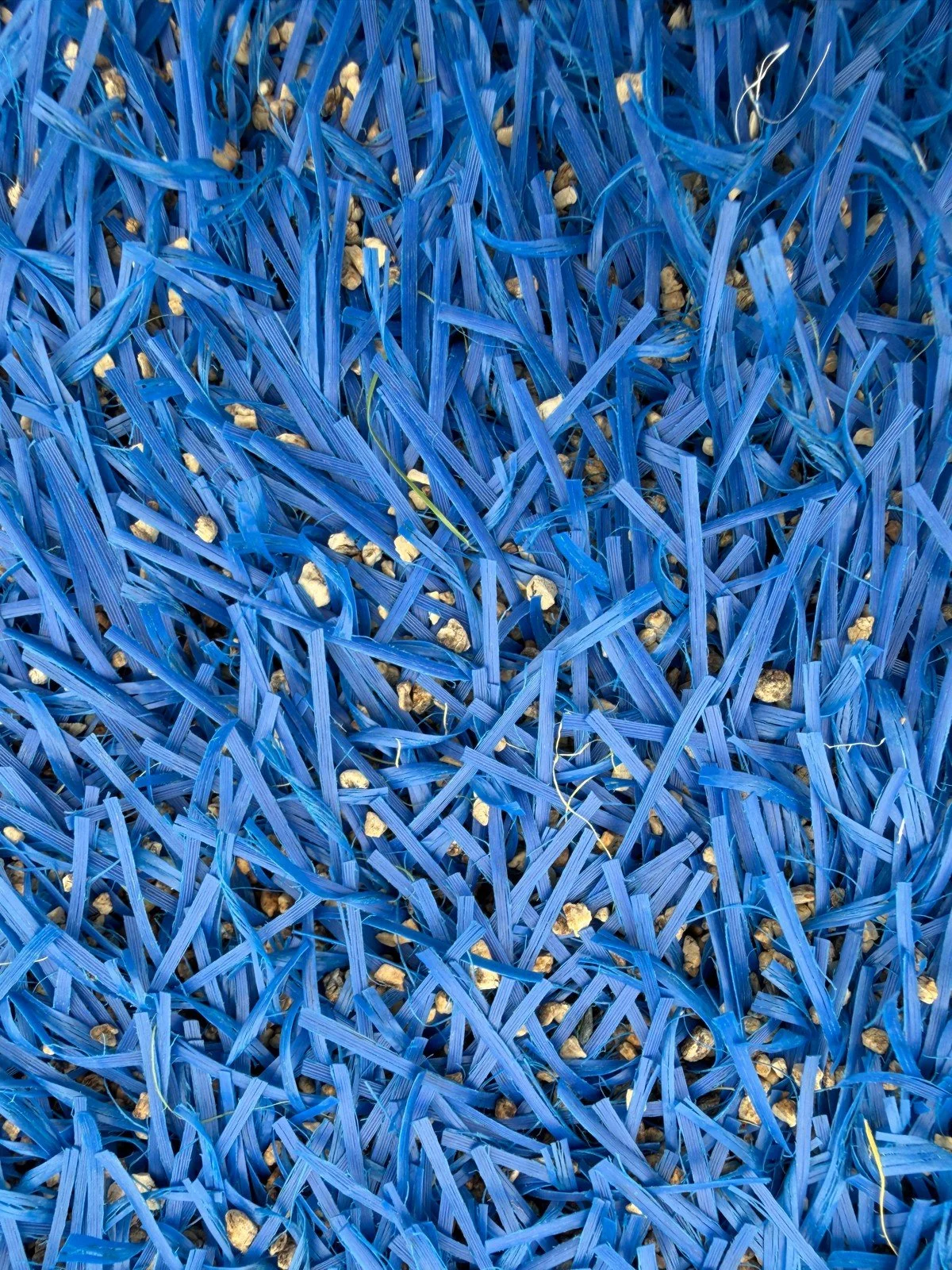 A closeup of cork infill used for this blue synthetic turf sports field.