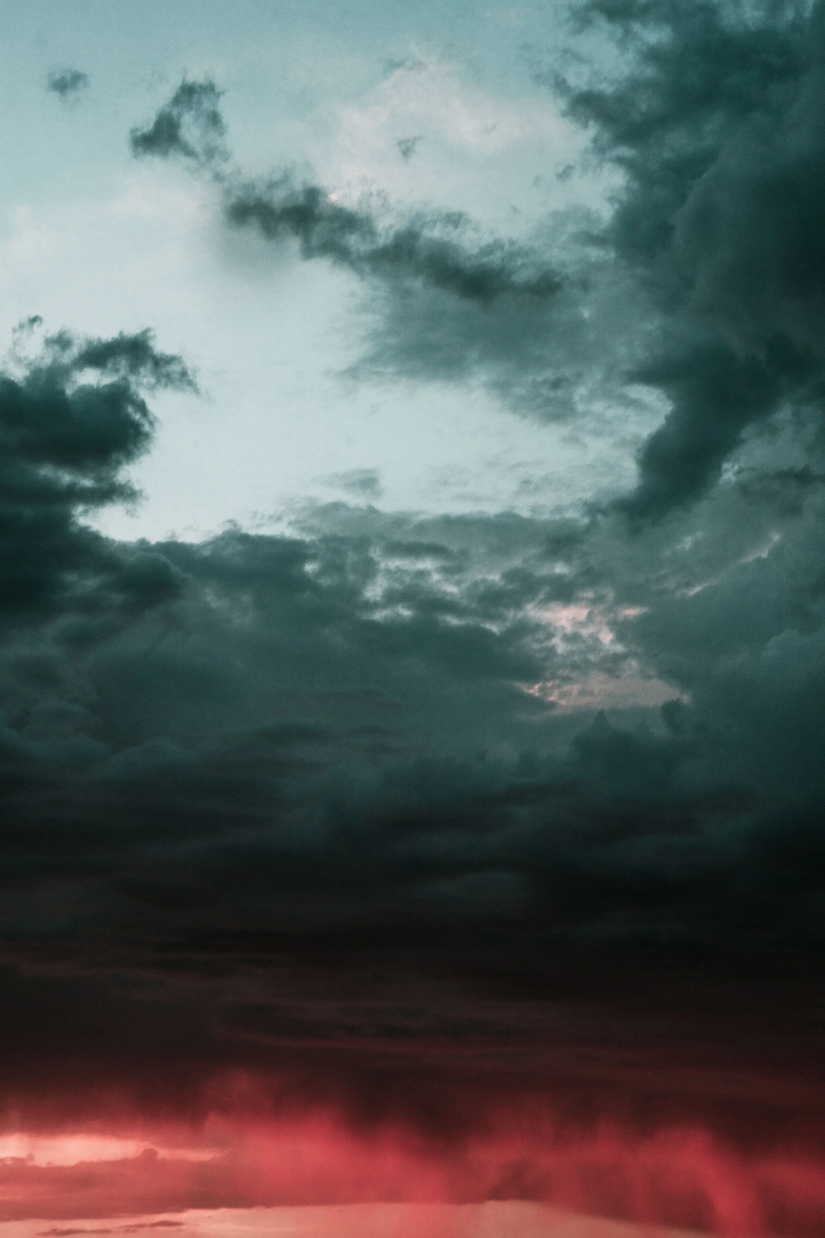 Dark grey teal clouds give way to sheets of falling rain illuminated by the bright red sunset below. Pocatello, Idaho.