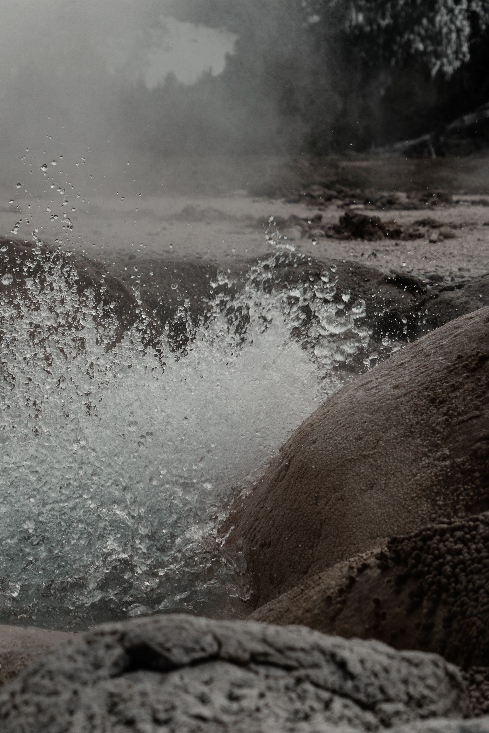 hot spring spraying boiling water whilst surrounded by its own fogy steam in brown mineral stone pool. Yellowstone National Park, Montana.