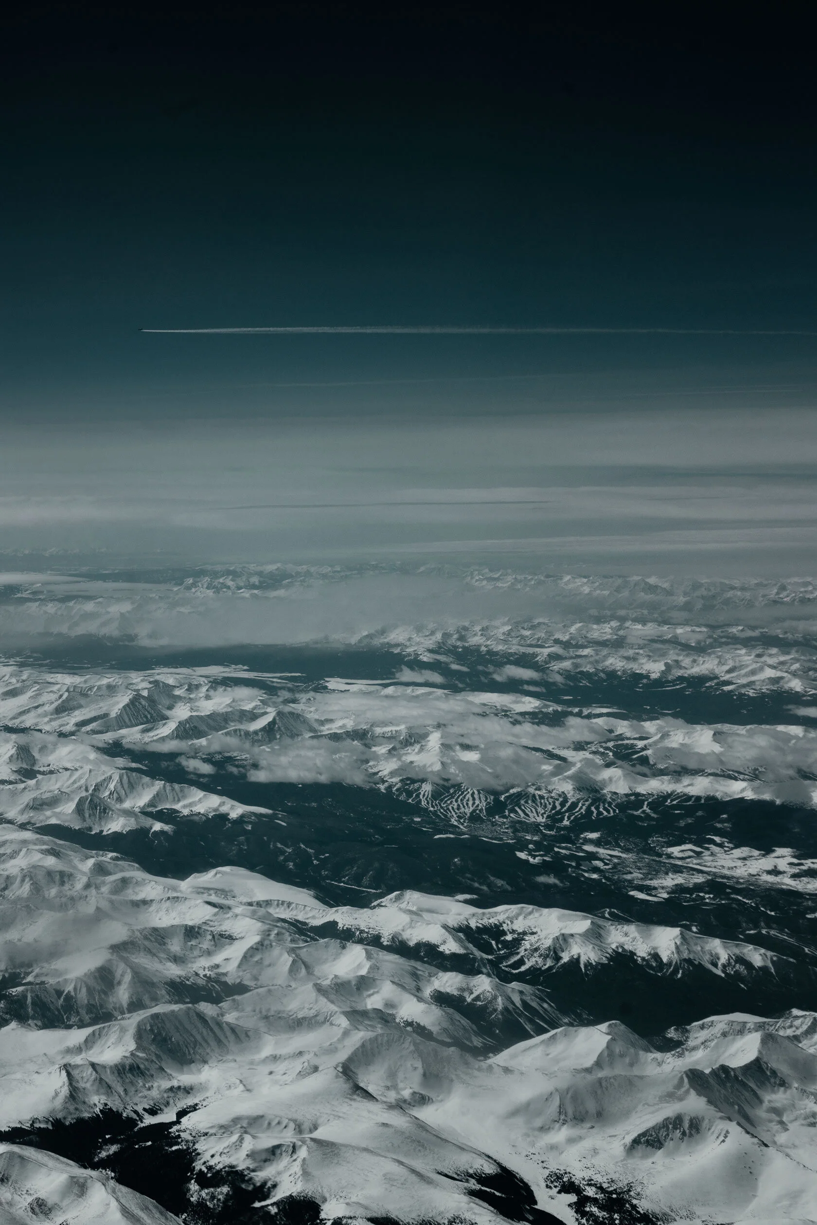 view from airplane window of another plane flying parallel, layer of clouds, and then seemingly endless snow capped mountains. taken over The Rocky Mountains, United States of America