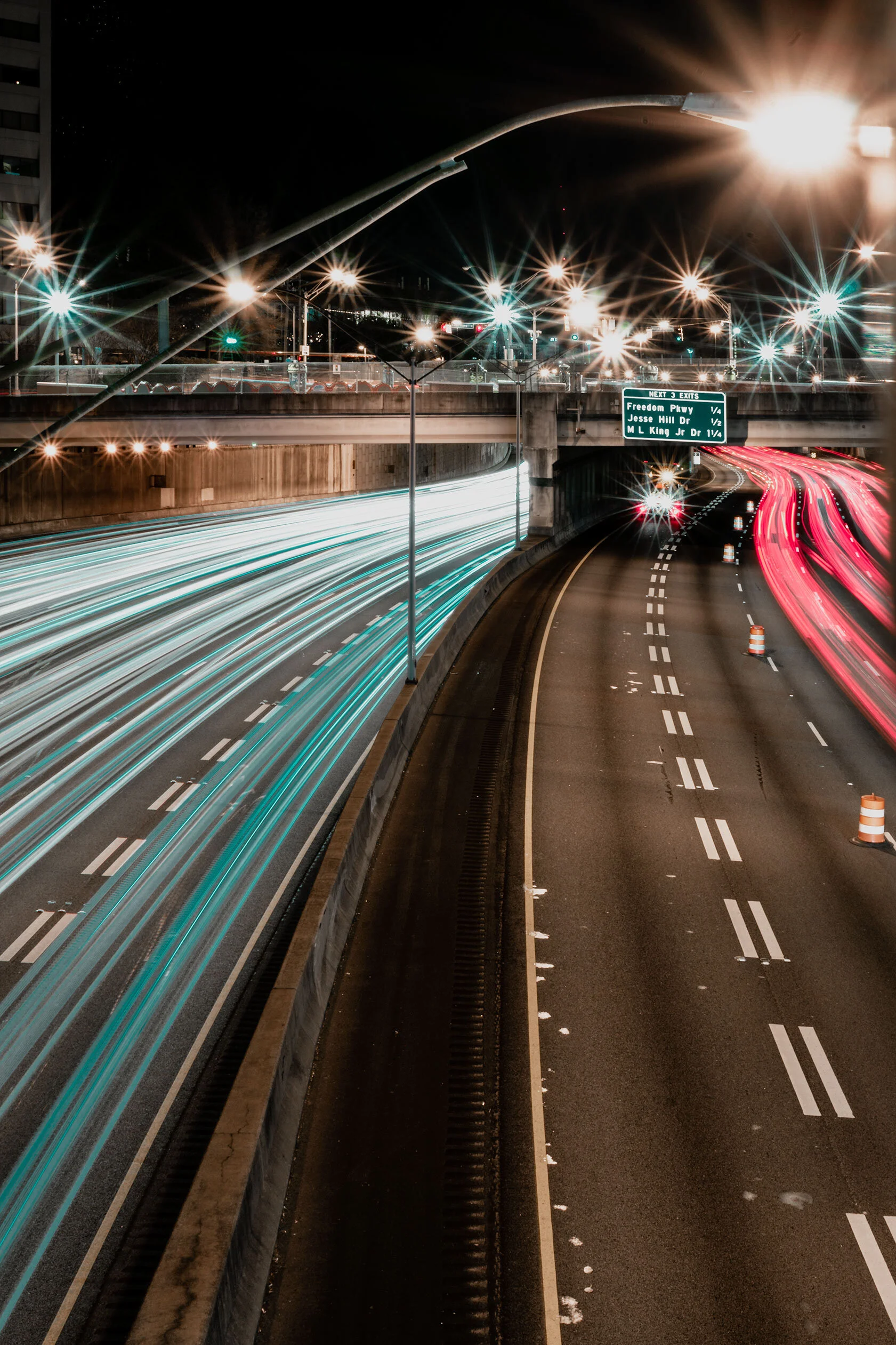Light trails of cars snake under overpass in Atlanta, Georgia. City lights create spiky flashes of copper and teal in this long exposure.