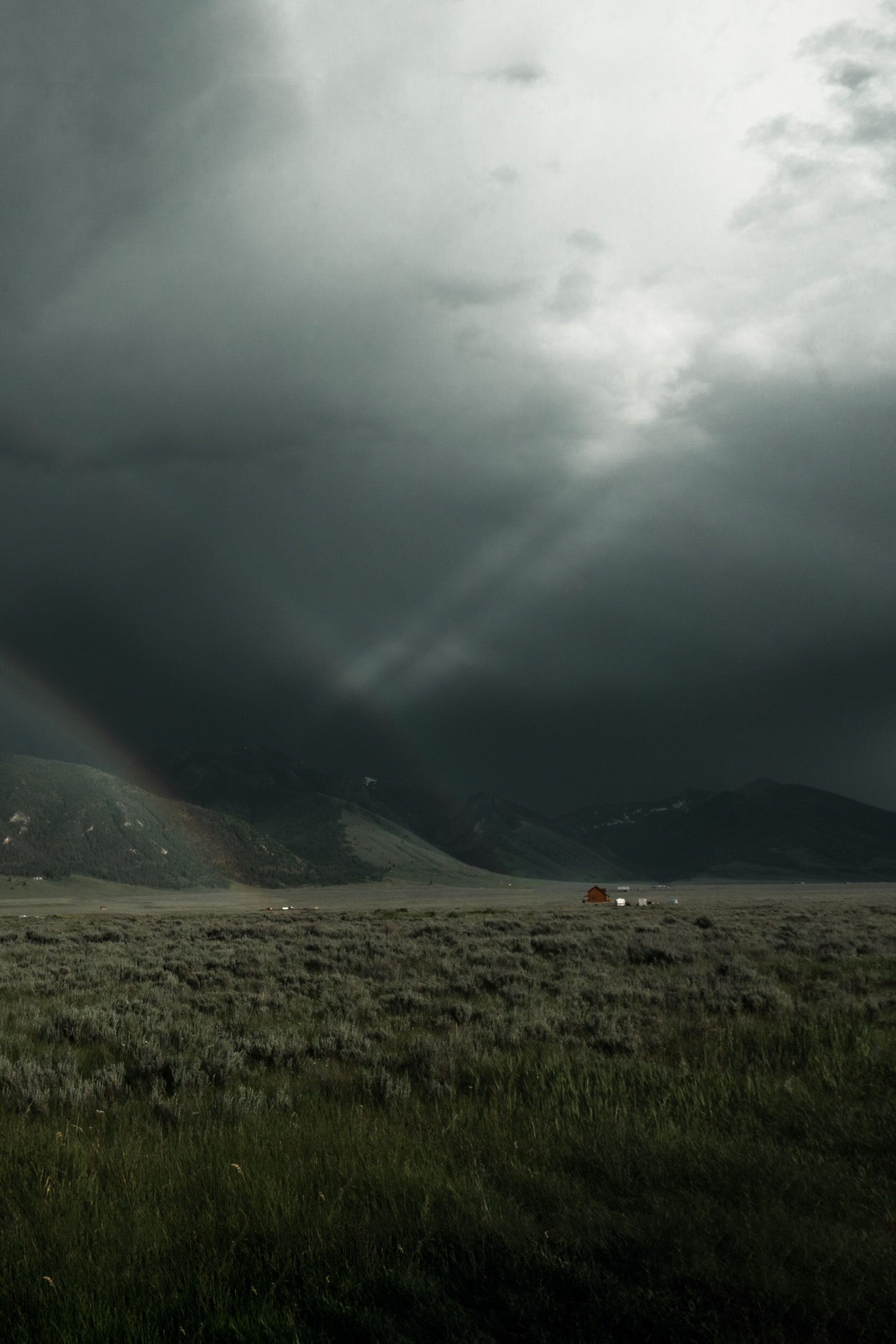 Double rainbow over red cabin and green grasslands. Rays of light shine through dark clouds over Island Park, Idaho.