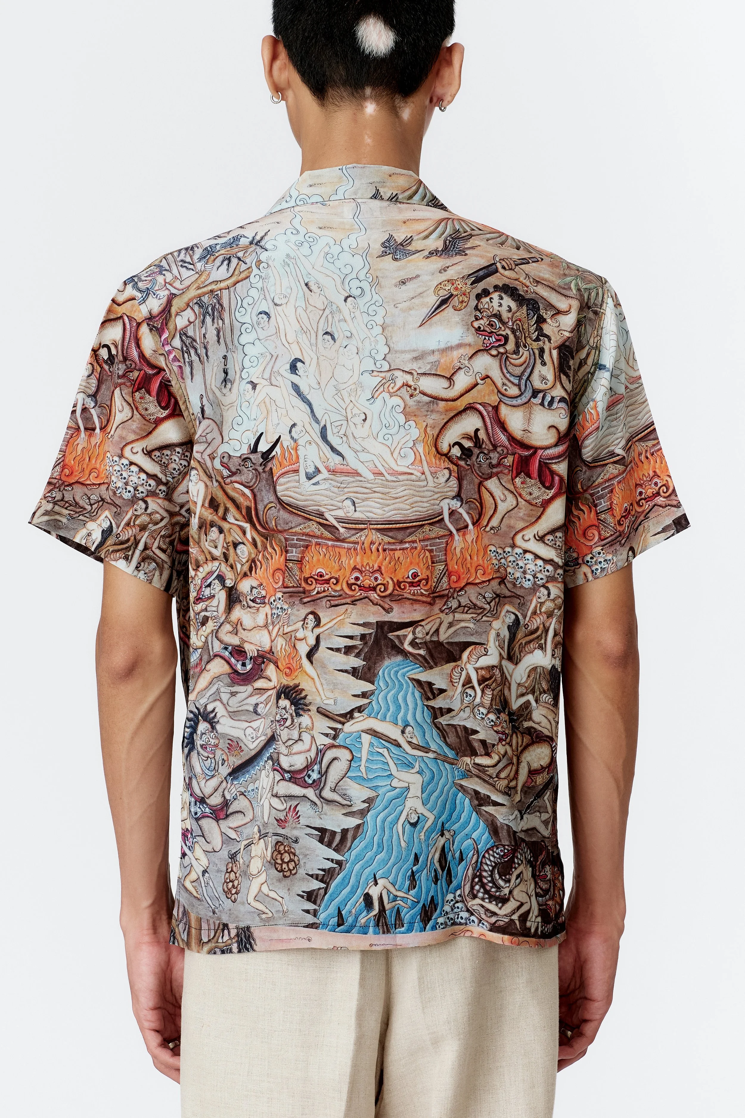Back view of Atma Penangsaran silk crepe short sleeve shirt displaying complex Balinese underworld illustration.