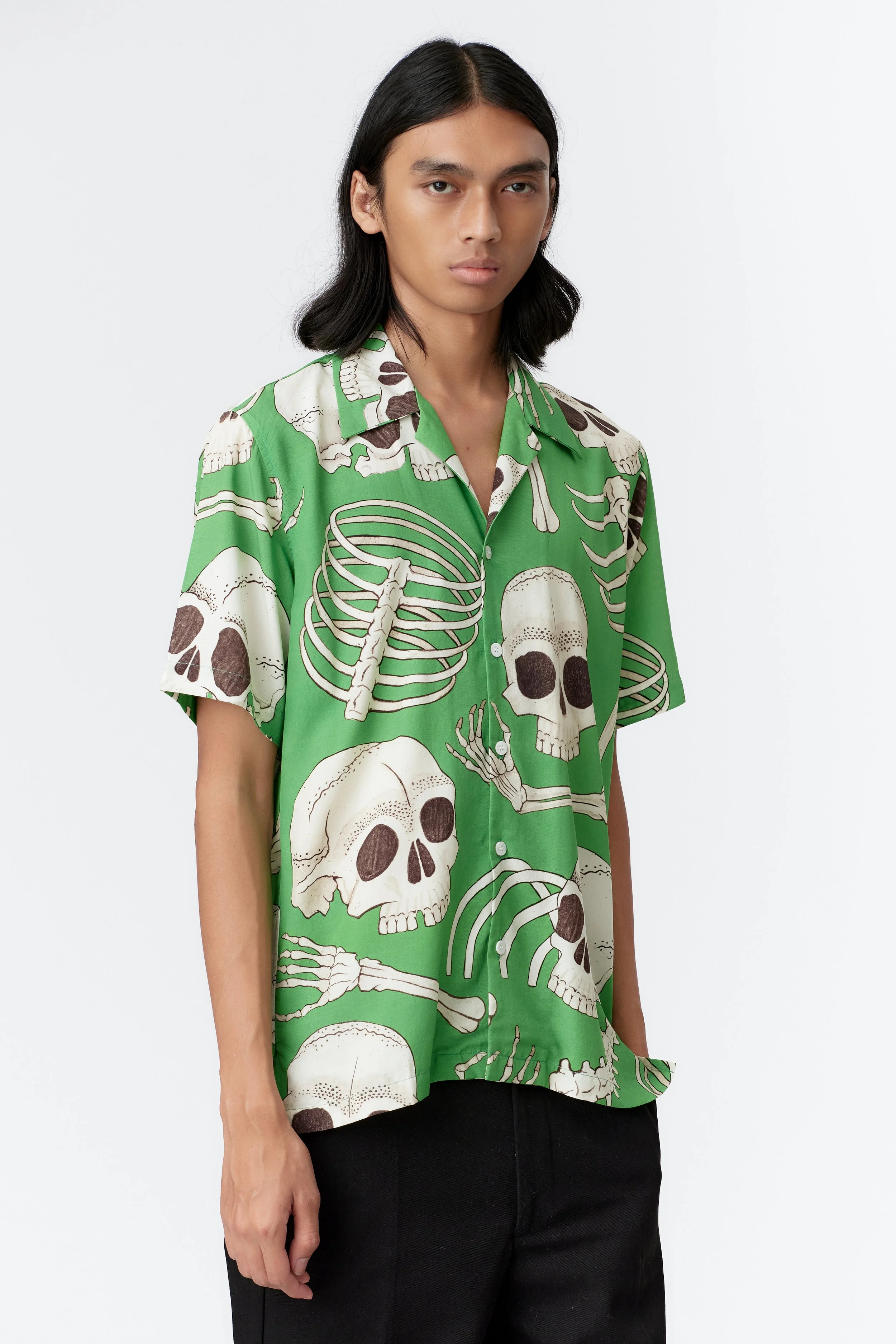 Three-quarter front view of green Skeleton camp collar shirt styled with black trousers