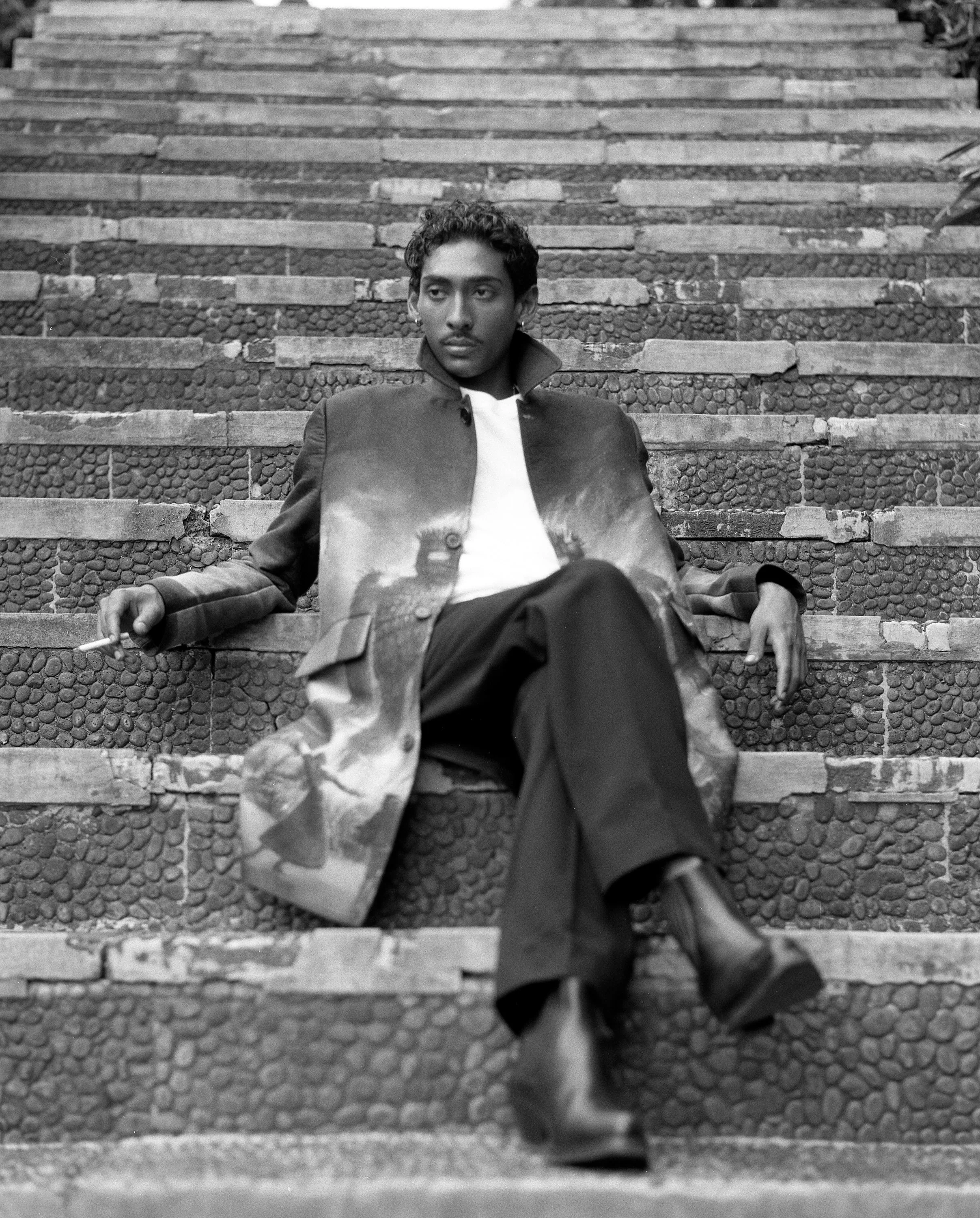 model sitting on steps of water palace wearing endless joy wickerman jacquard woven overcoat