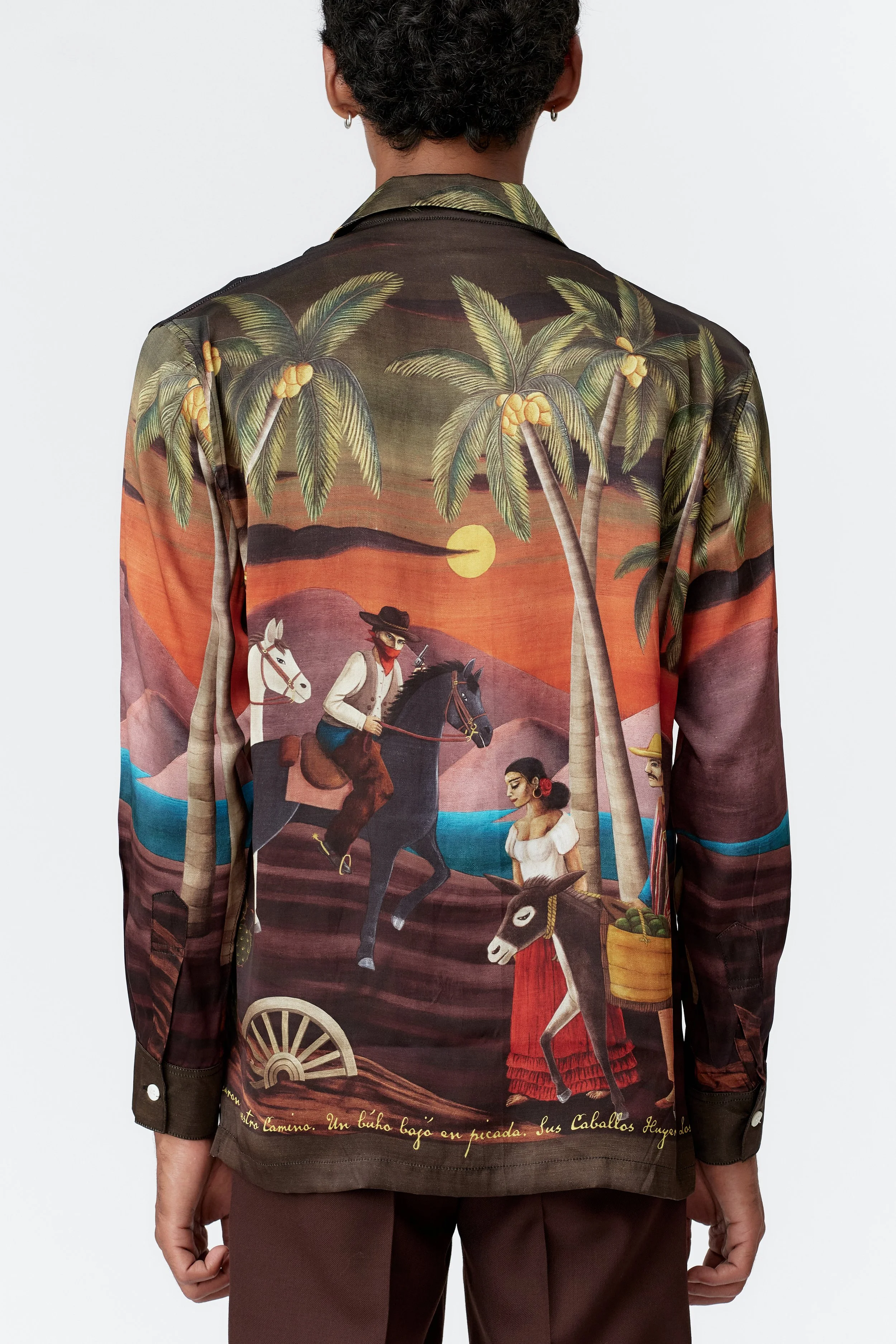 Back view of bottle green silk shirt showcasing Western-inspired landscape with palm trees and molten orange sky.