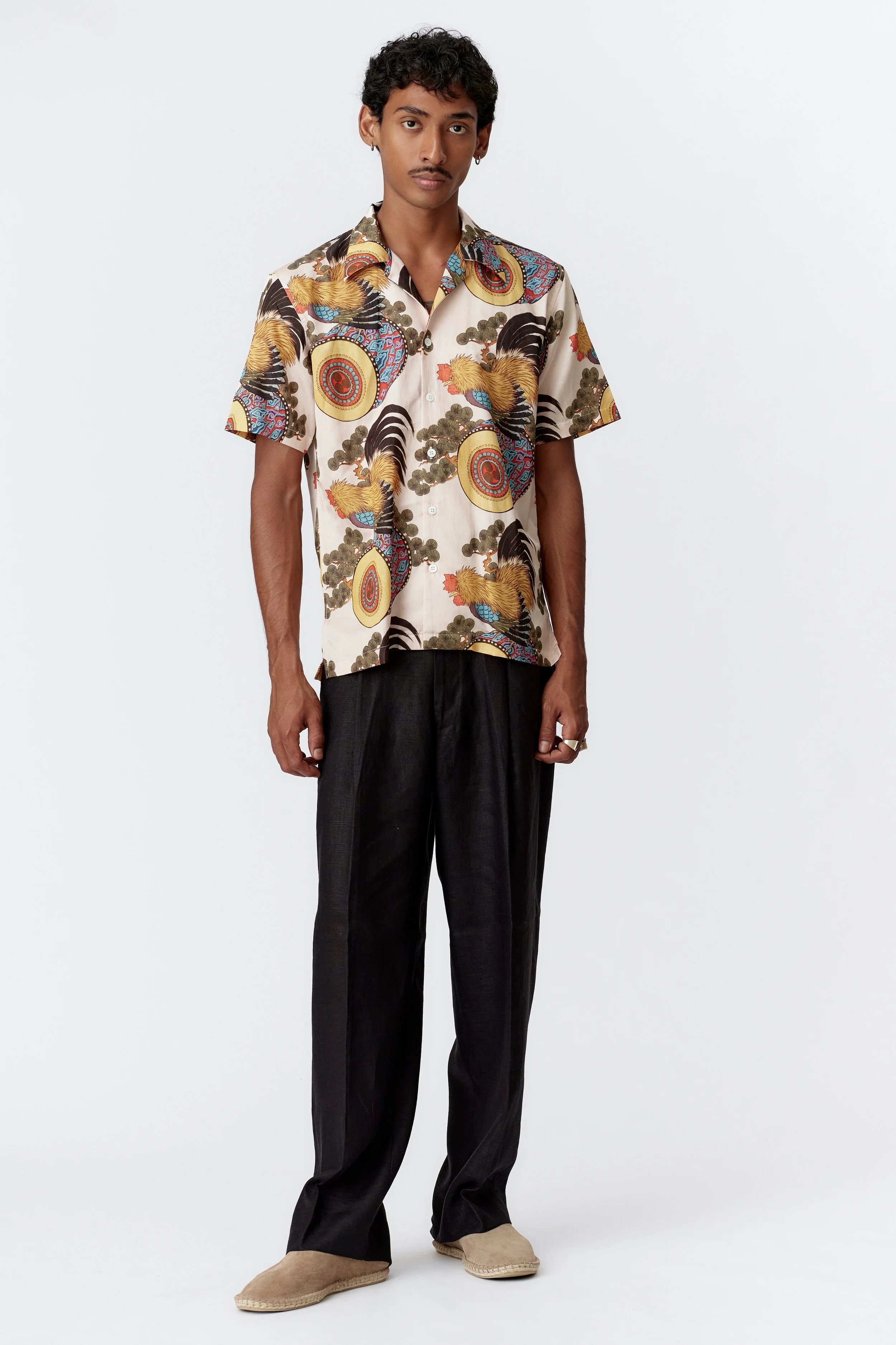 Full body view of model styling cream silk cotton rooster print shirt with black trousers