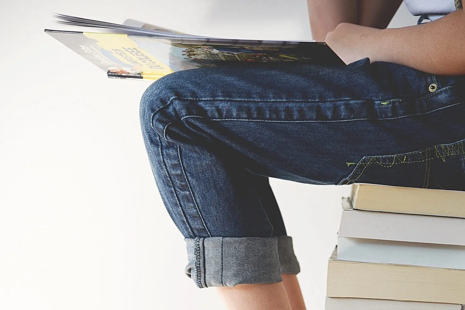 Person seated on stack of books, close-up of bare feet and jeans