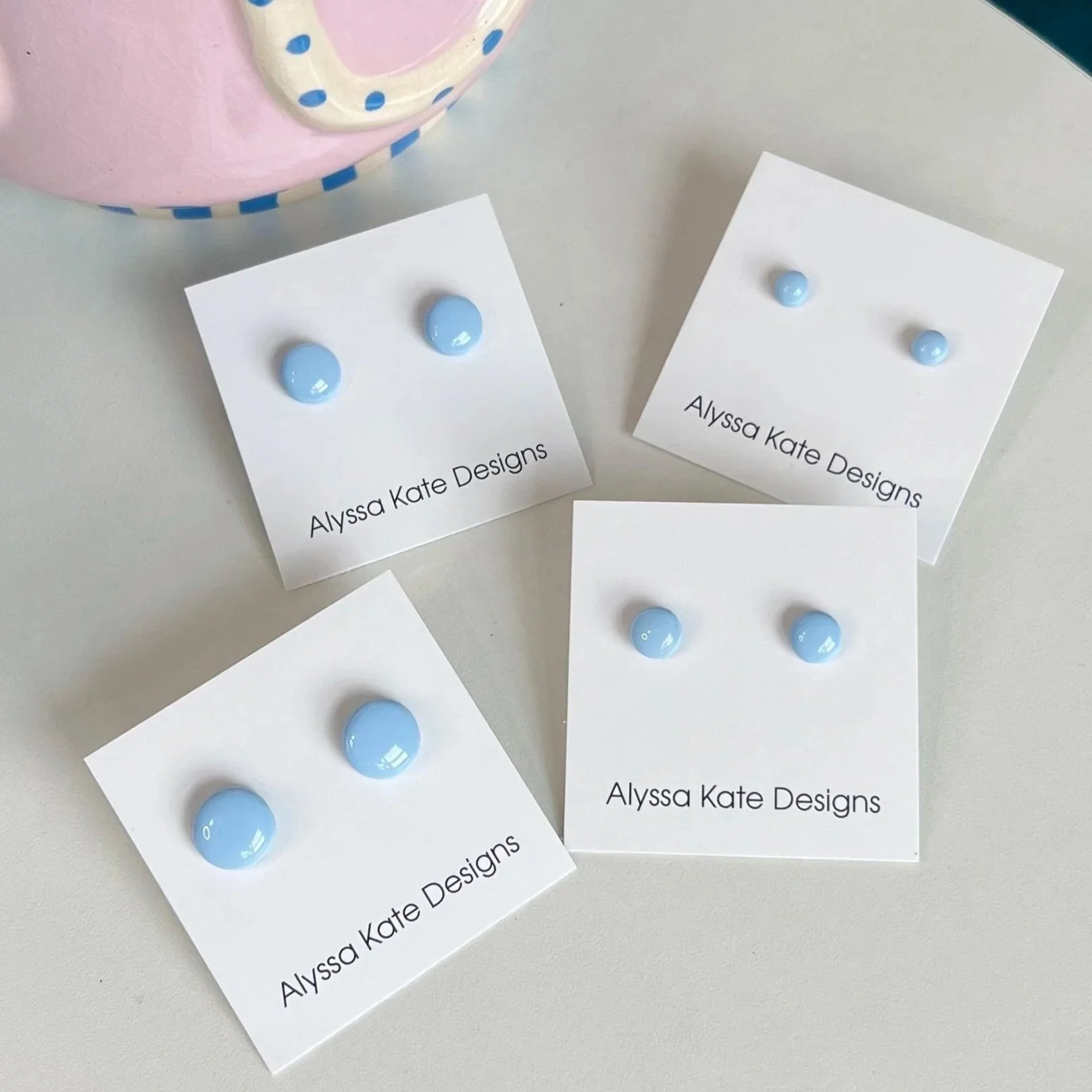Baby blue polymer clay stud earrings displayed in multiple sizes on Alyssa Kate Designs jewelry cards.