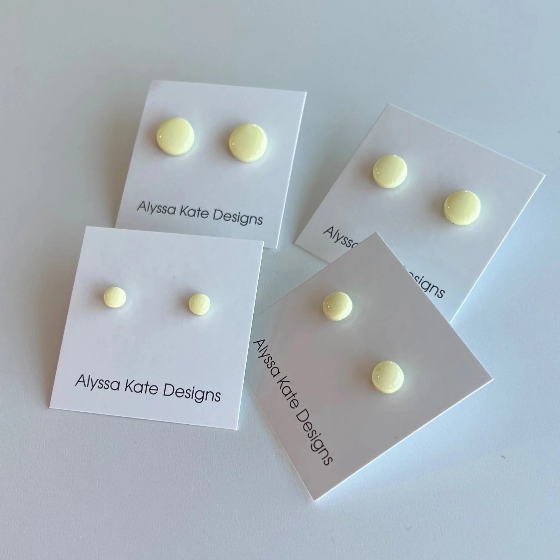 Butter yellow polymer clay stud earrings displayed in multiple sizes on Alyssa Kate Designs jewelry cards.