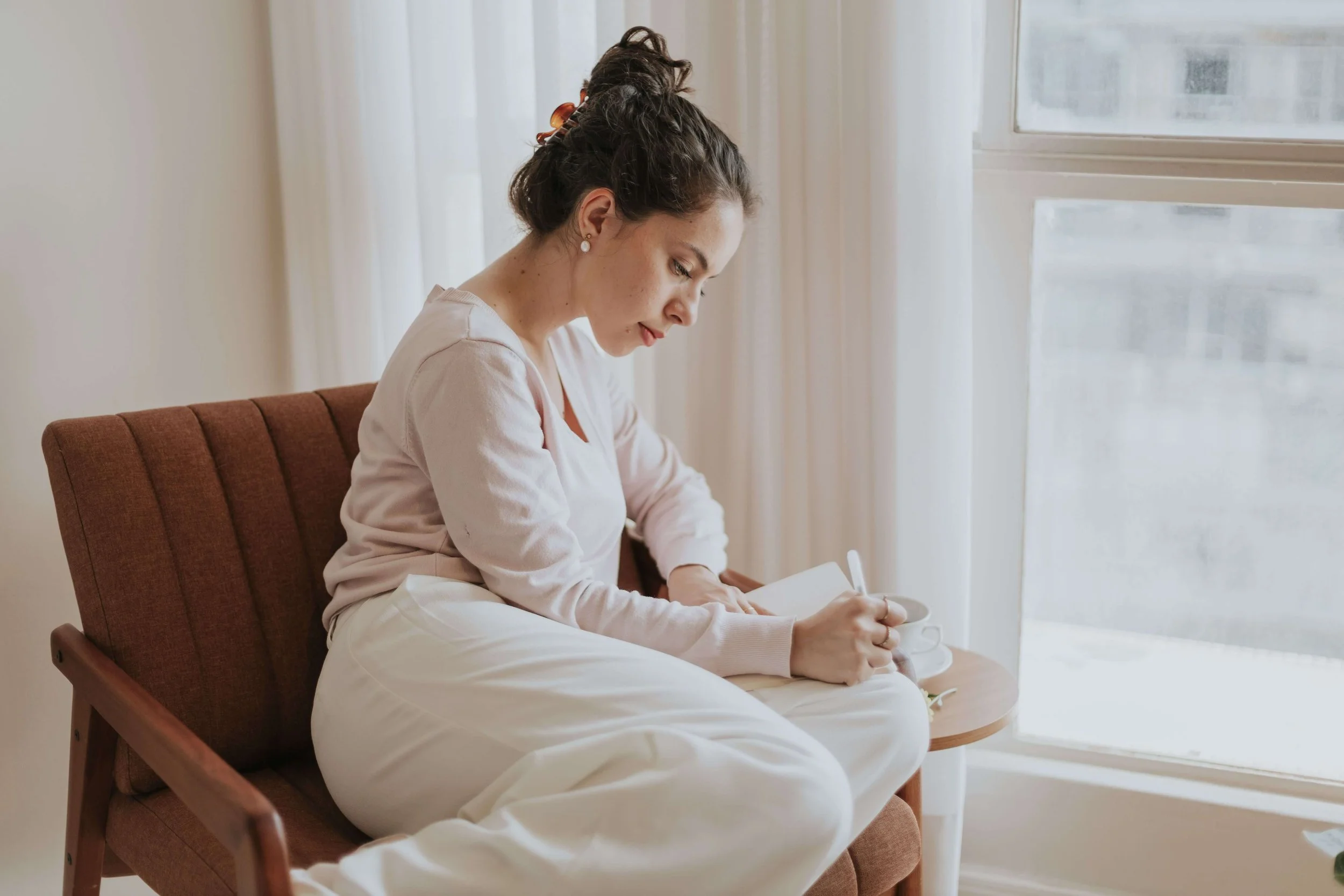 Woman journaling by a window as she reflects on building healthier money habits and greater financial confidence.