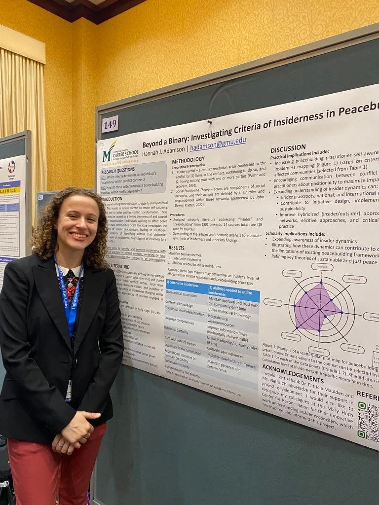 Hannah Adamson standing in front of her poster titled, "Beyond a Binary: Investigating Criteria of Insiderness in Peacebuilding" at NCUR