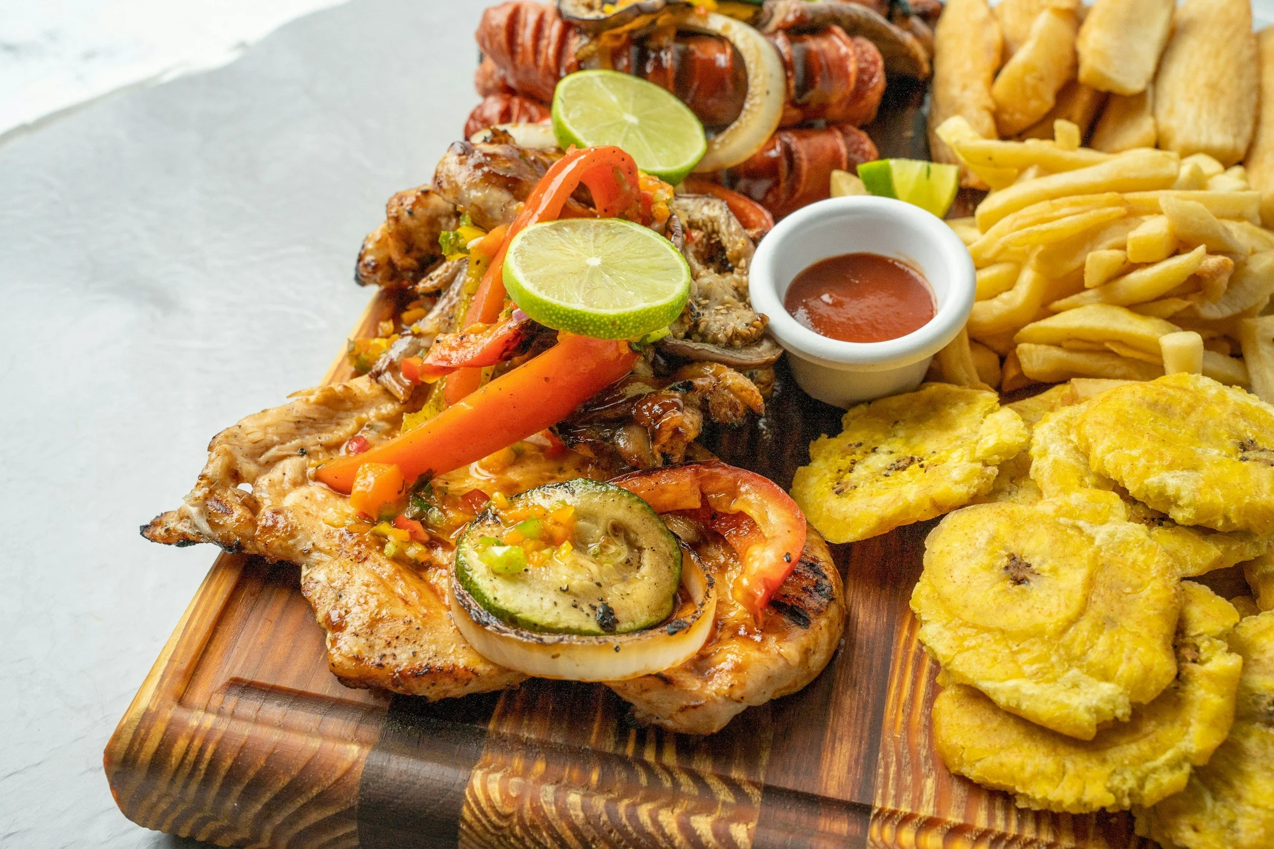 Grilled chicken and plantains on a wooden slab.