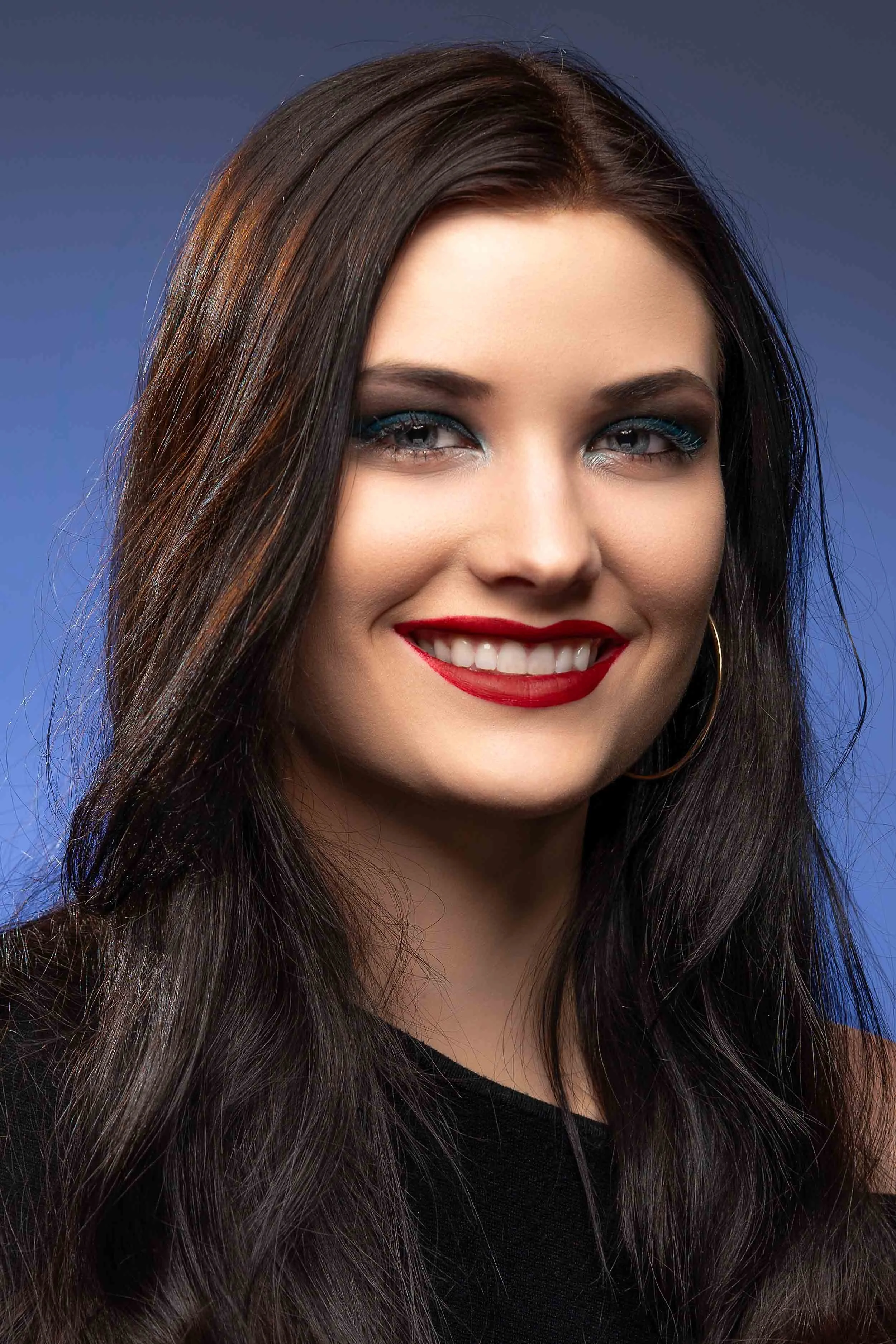 Professional fashion headshot of a woman with red lipstick and blue eyeliner against a blue background, shot by a South Bend photographer.