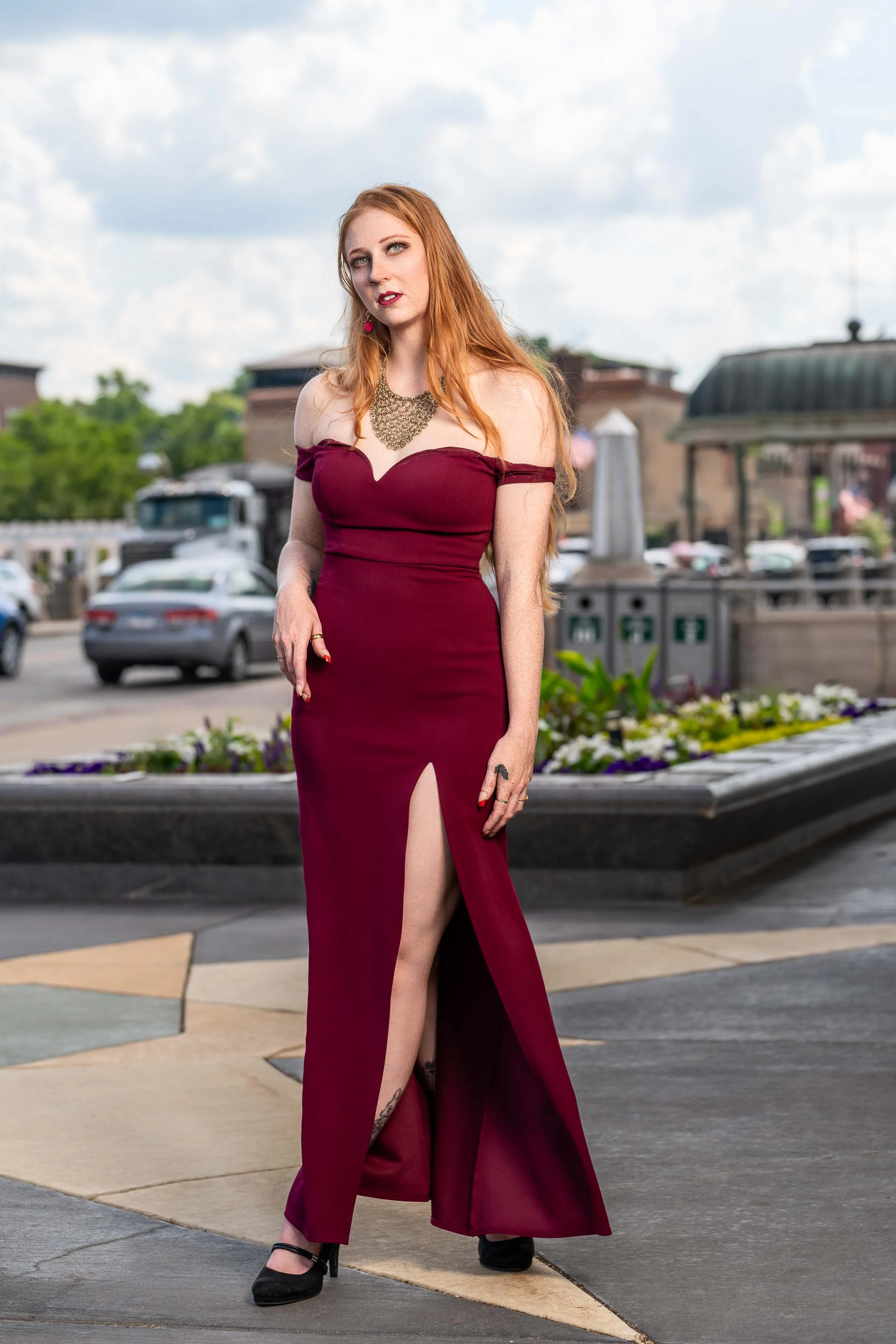 Full-length lifestyle portrait of a redhead model in a maroon formal gown with a high slit, shot in downtown South Bend, Indiana by James Russell Photography.