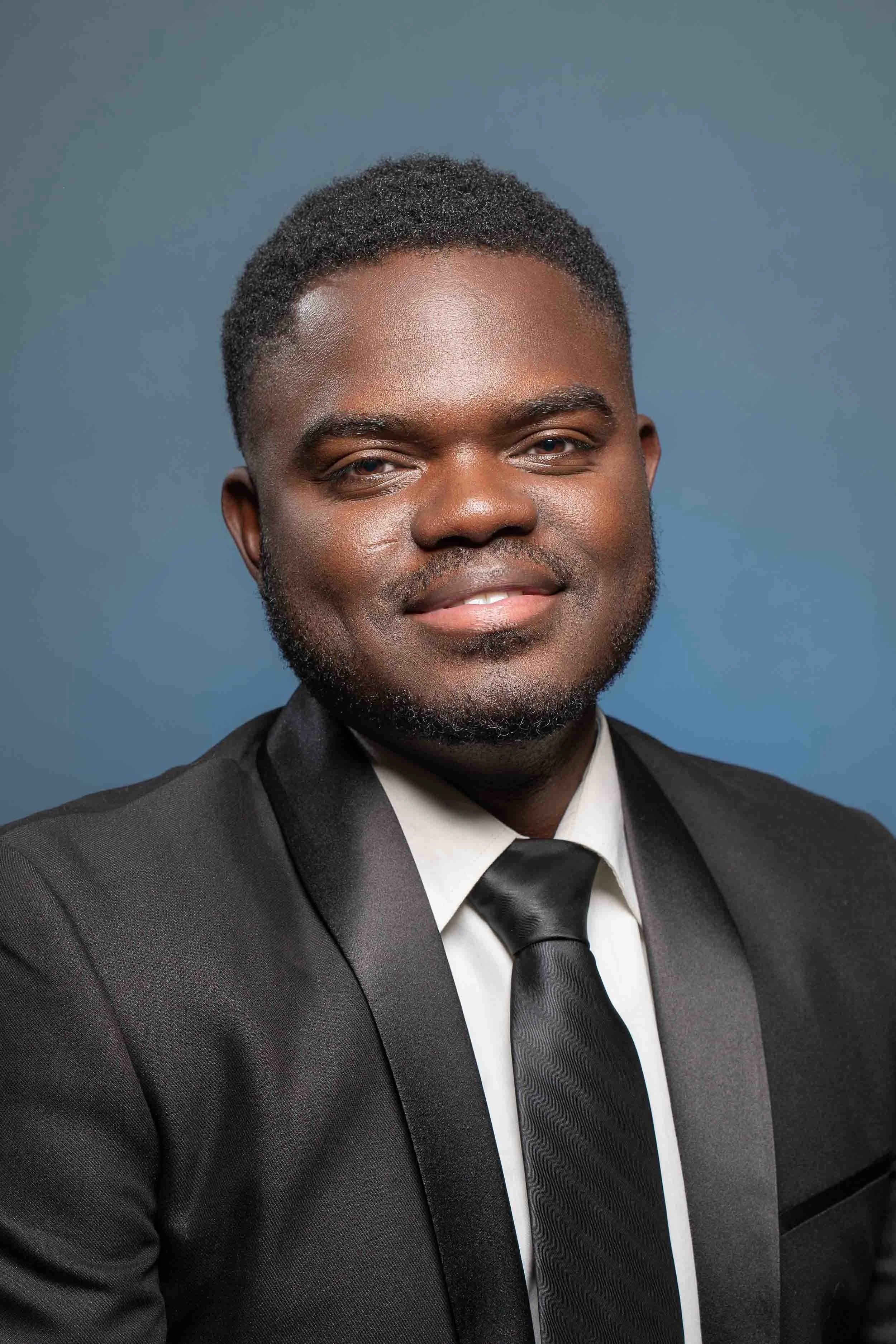 Formal business headshot of a man in a black suit and tie against a blue background; professional studio photography by a South Bend headshot photographer