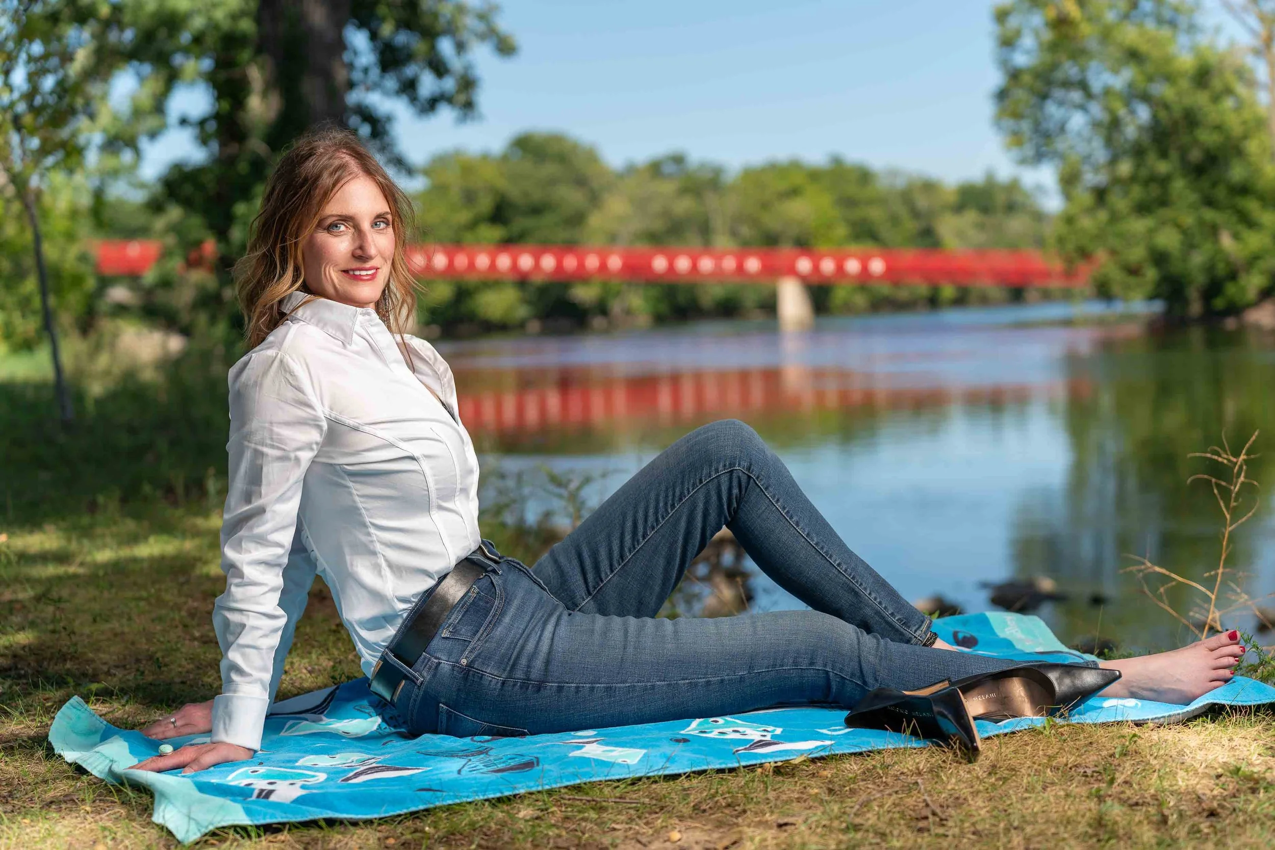 Outdoor lifestyle portrait of a woman in a white button-down shirt and jeans relaxing by a river in the Michiana area.