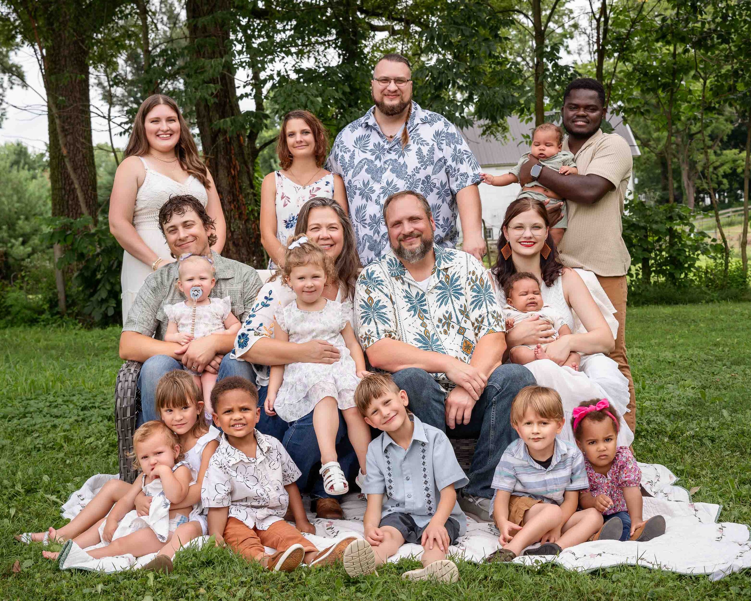 A large multi-generational family group posing for a portrait outdoors on a quilt in a grassy field in South Bend.
