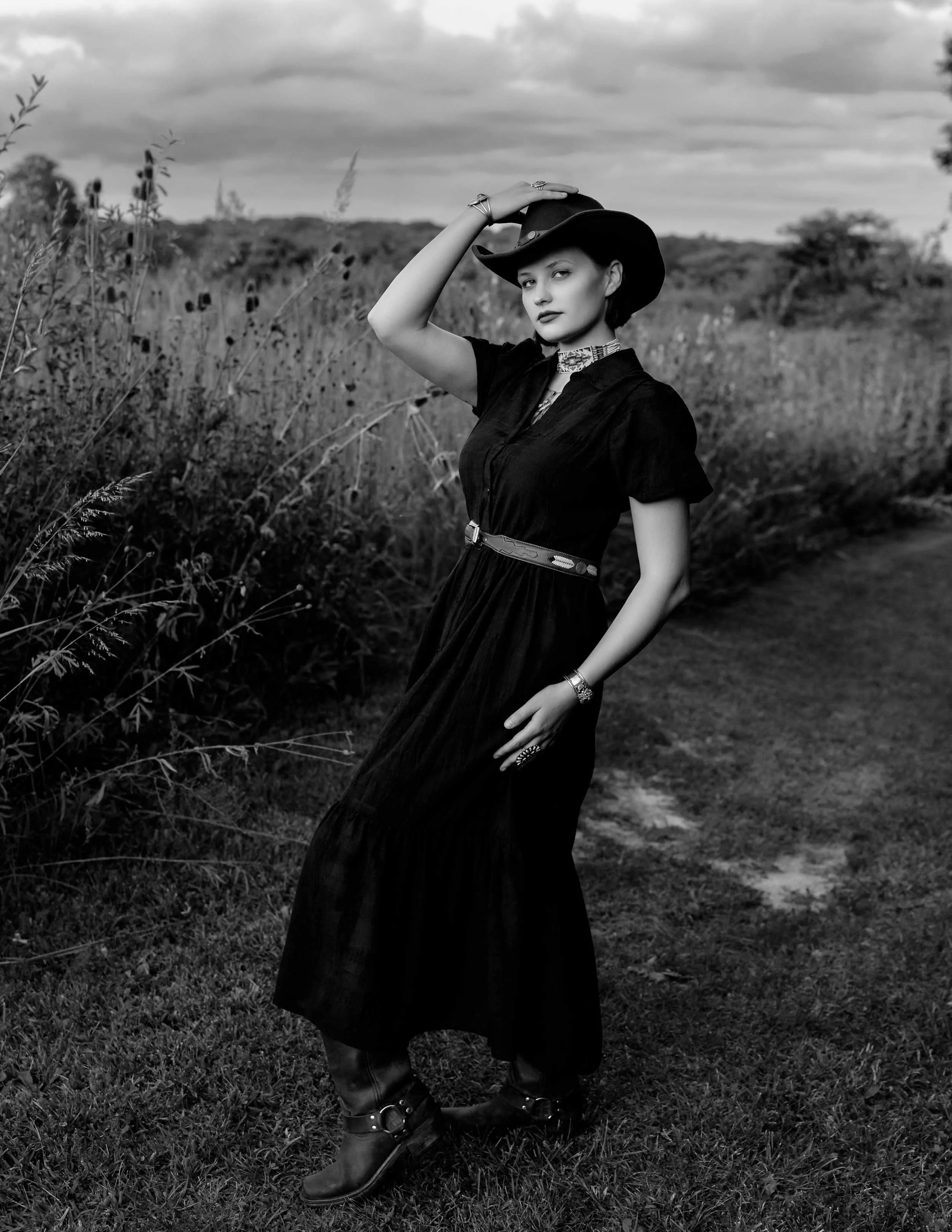Fine art black and white outdoor fashion portrait of a woman in a black dress and cowboy hat in a Southern Michigan meadow.