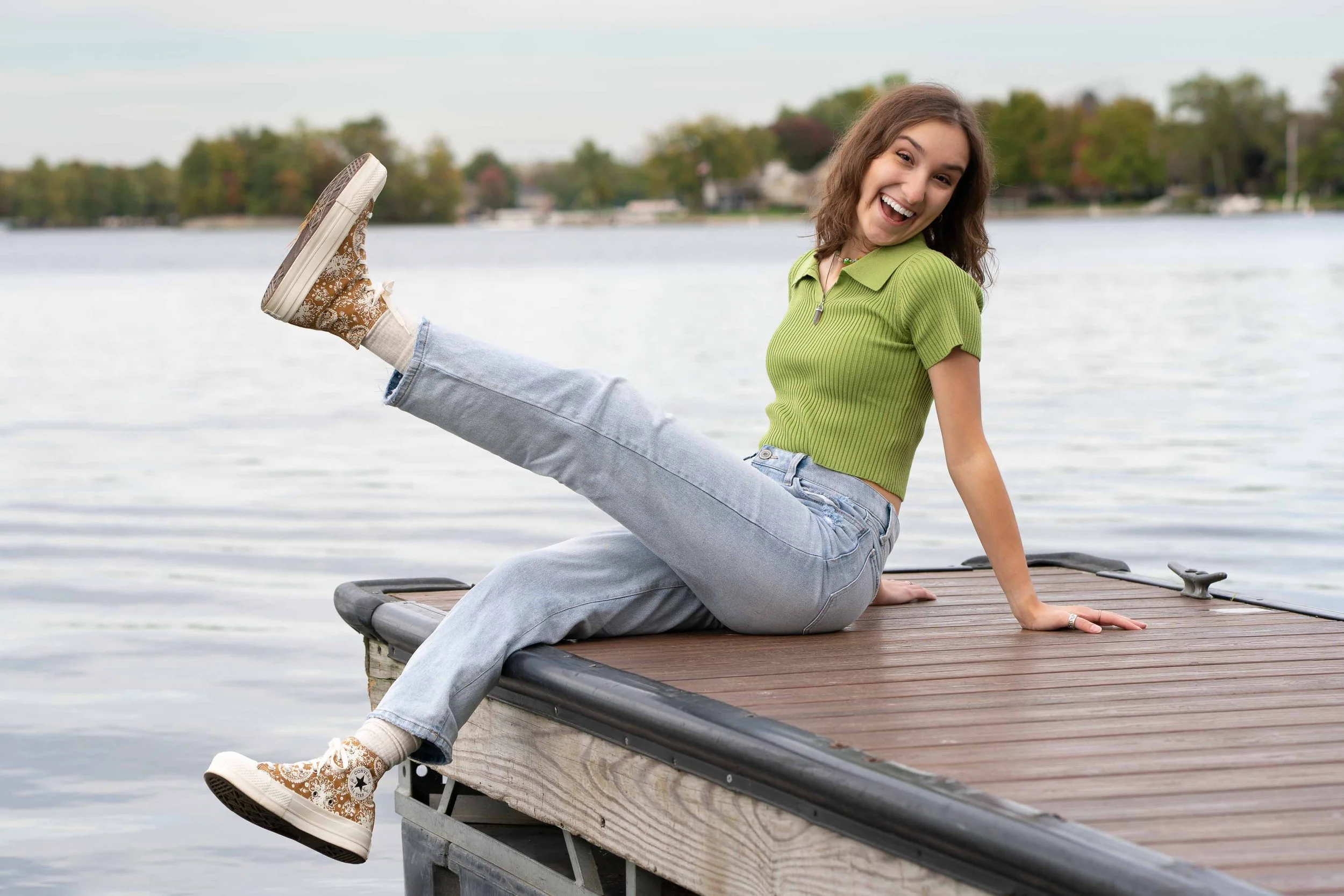 Senior lifestyle portrait of a happy teenage girl sitting on a dock by the St. Joseph River in Mishawaka, Indiana.