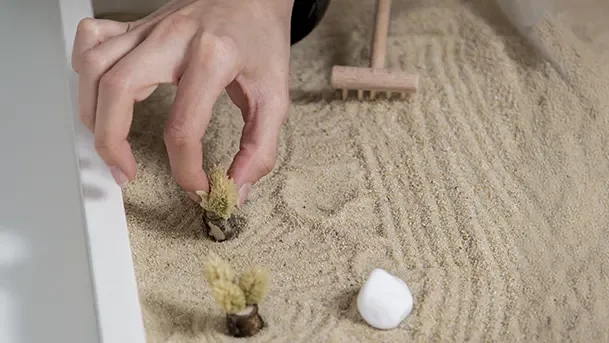 Hand arranging miniature objects in a sand tray during therapy, illustrating emotional expression, symbolic play, and therapeutic exploration through sand tray therapy.