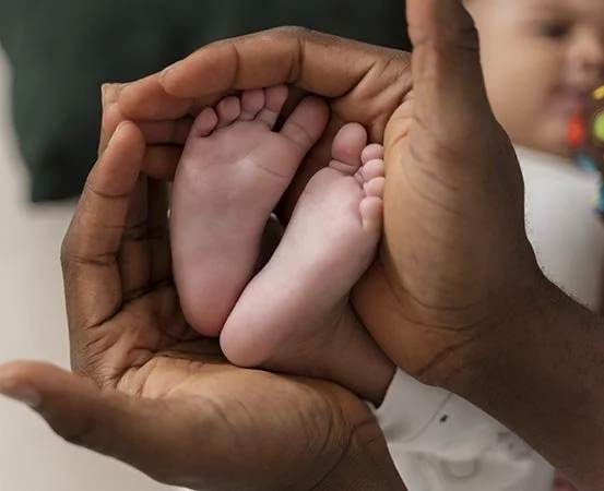 Close-up of a baby’s feet gently held in a parent’s hands, representing neonatal comfort, parental touch, safety, and pain relief through connection and soothing care.