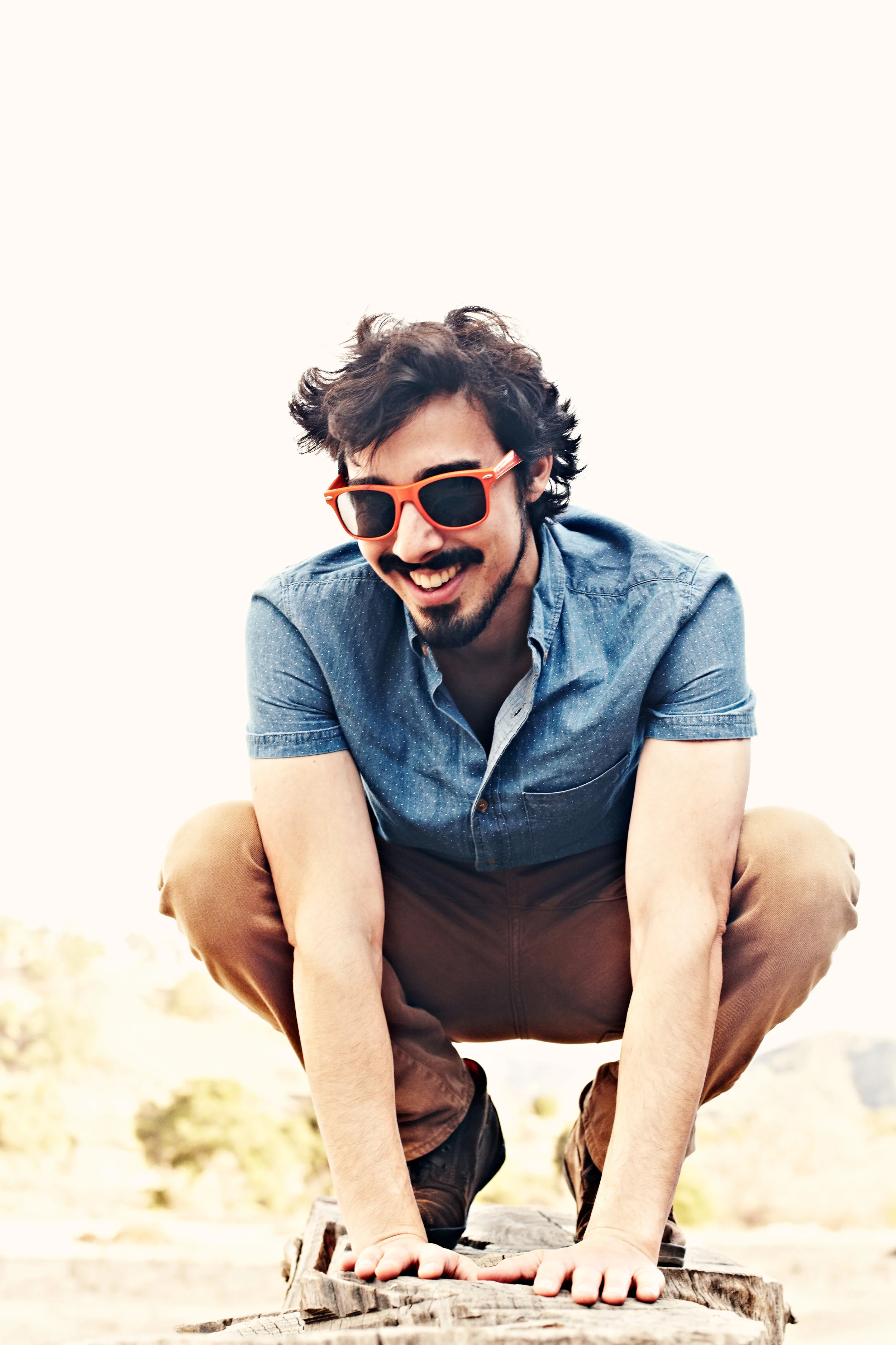 Young man in bright sunglasses crouching on tree stump
