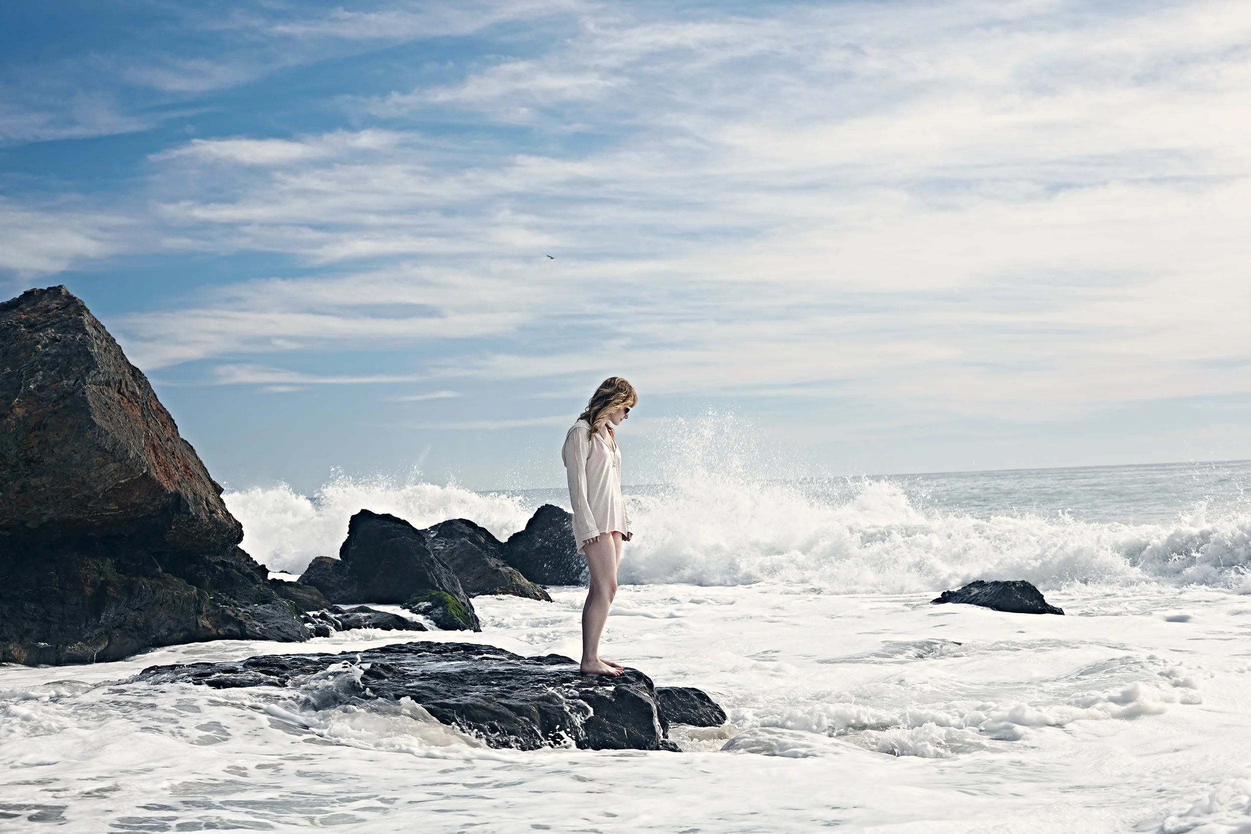 Young woman standing alone on a rock in the ocean