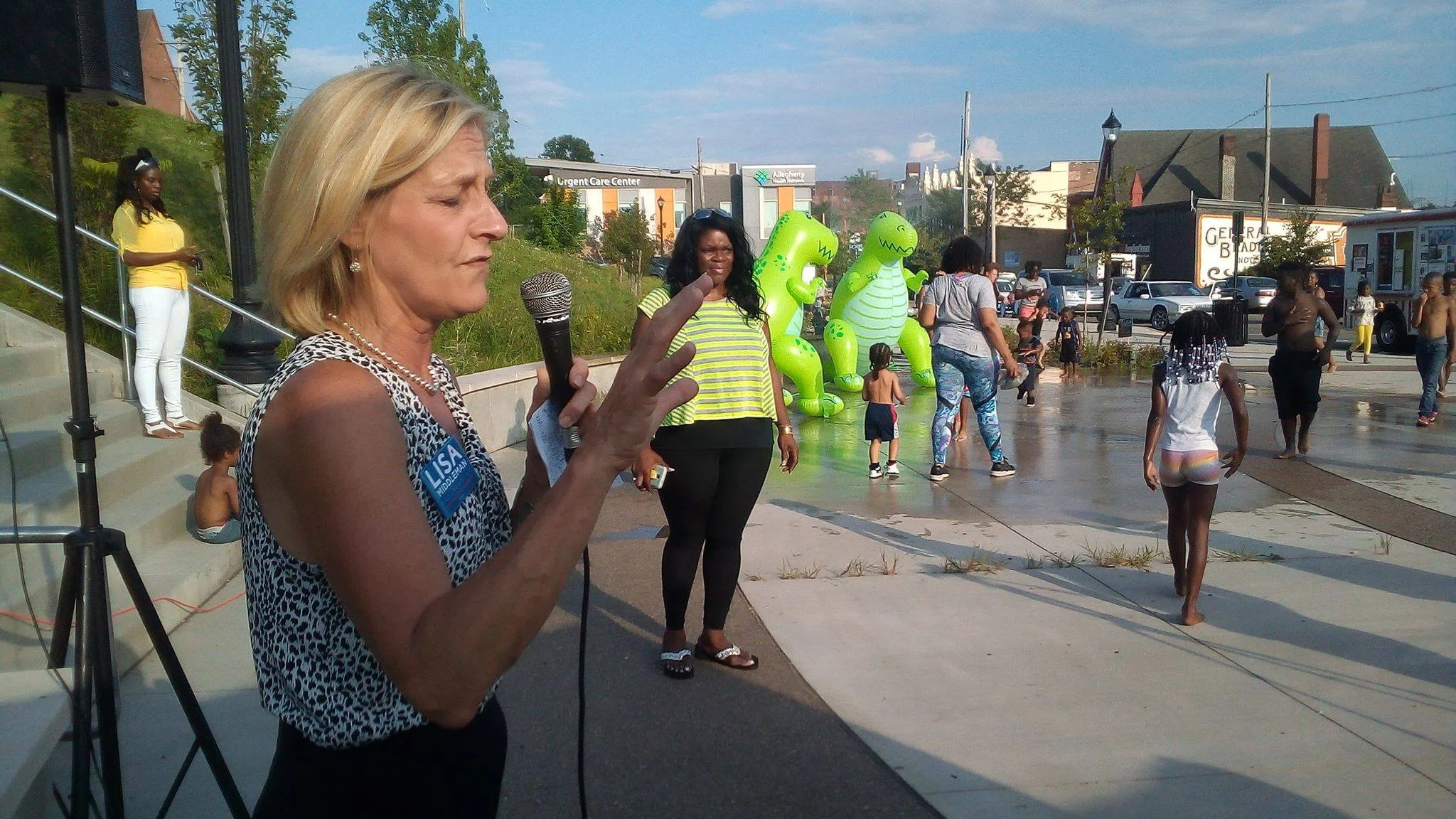 Lisa holding a microphone and speaking to a group of people on a Summer day.
