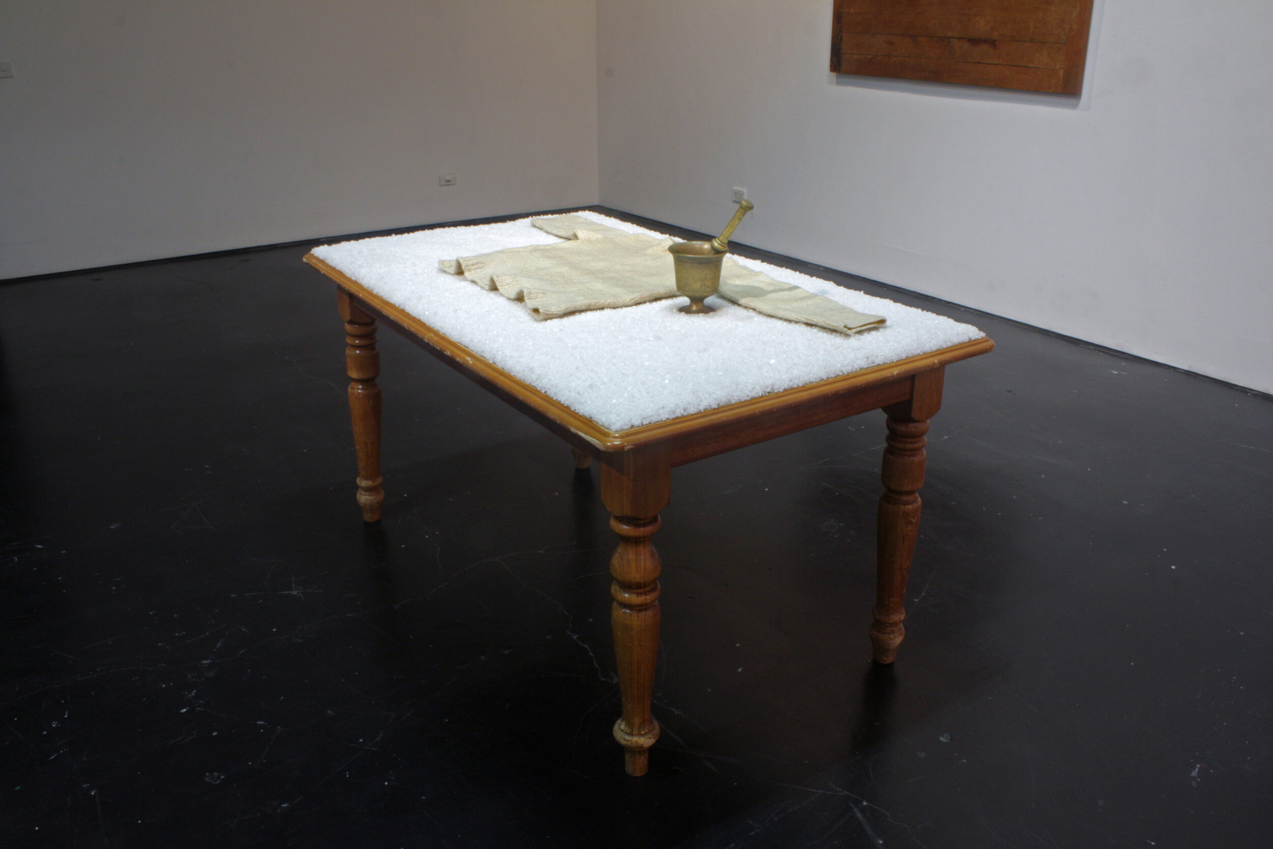    My sister’s table, my father’s garment, my mother’s mortar and pestle   ,  2013  Material: wooden table, granular salt, woolen handknitted garment, brass mortar and pestle. Presence: artist’s mother, father, sister, islands. 