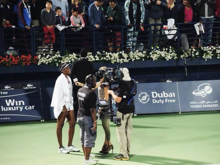 Camera crew setting up an interview at a tennis court