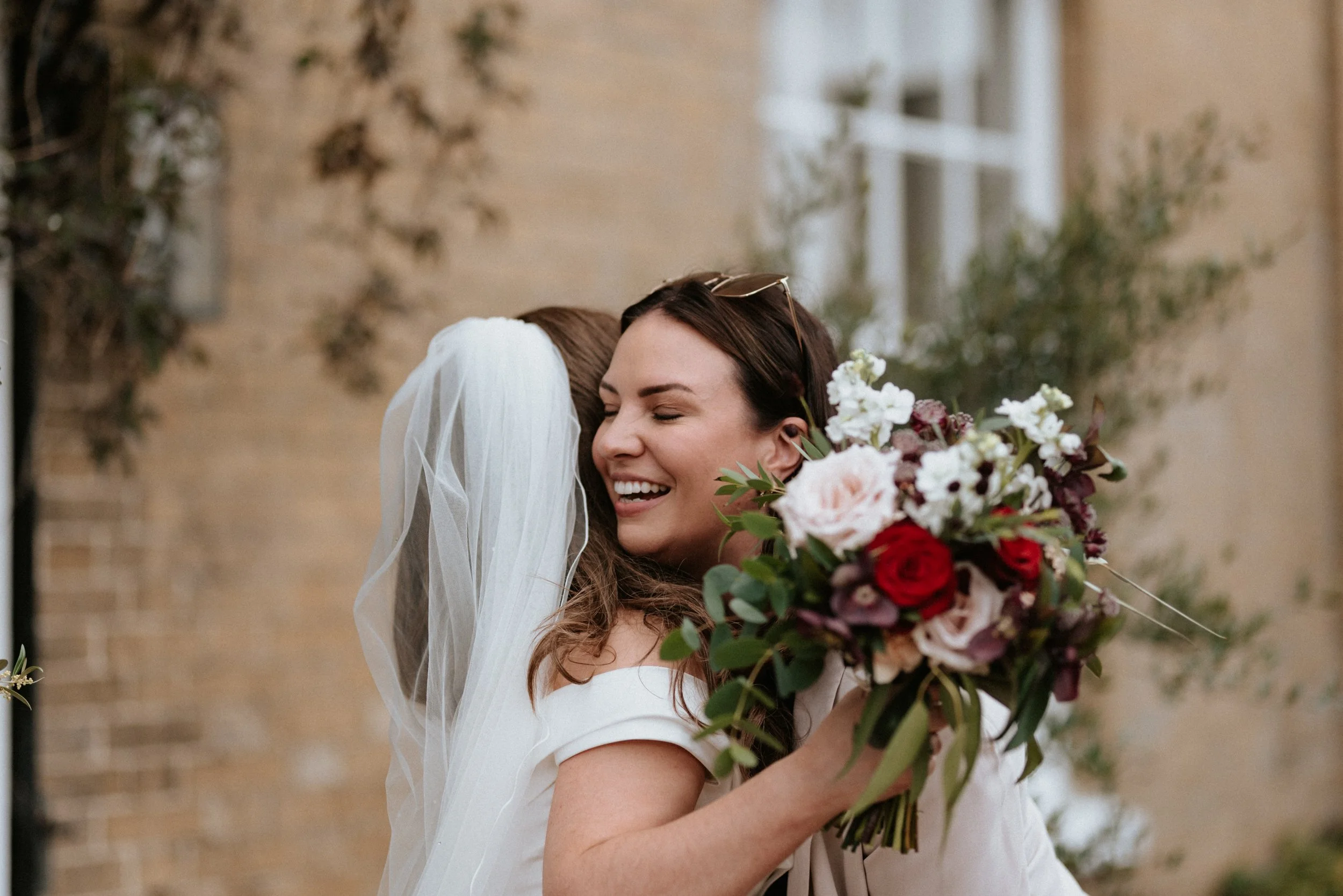 A happy bride at Godwick Great Barn, a Norfolk Wedding Venue,  hugs her Bridal Makeup Artist on her wedding day