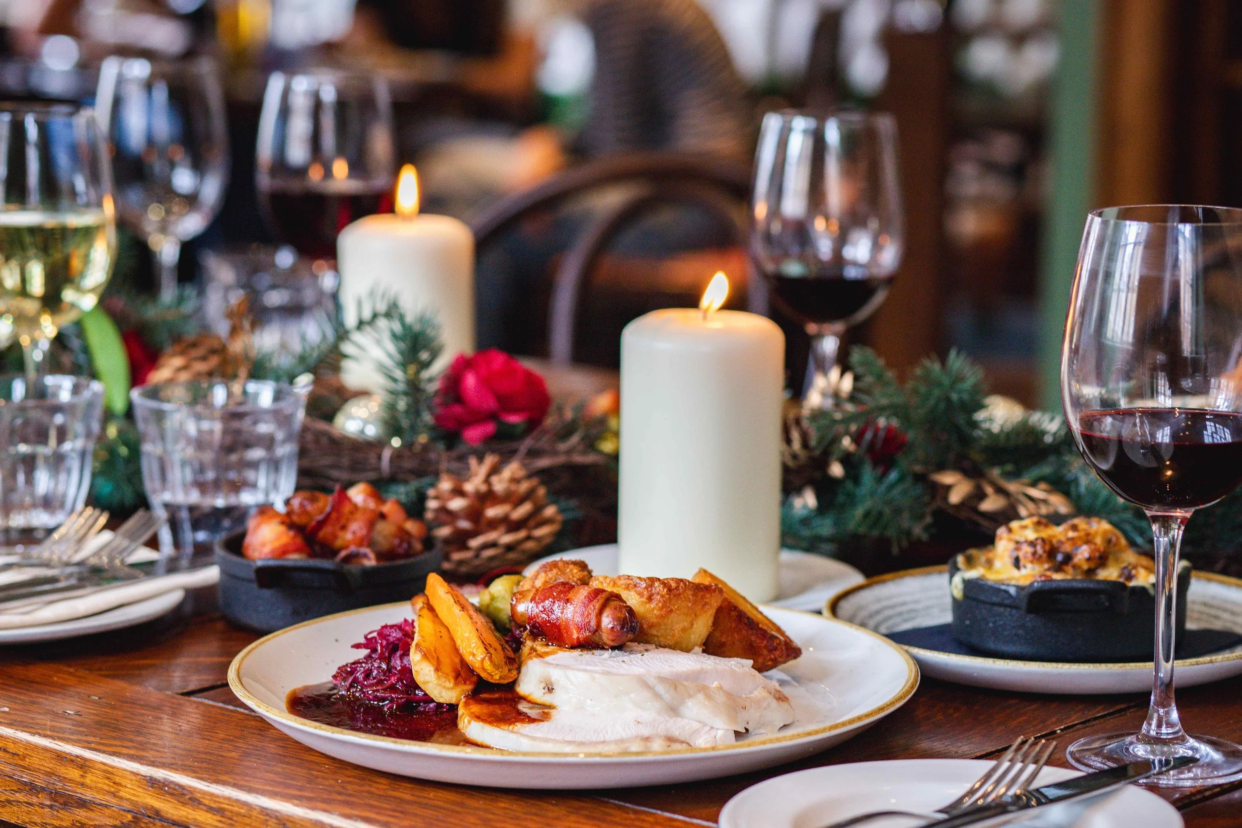 Festive holiday dinner table with roasted turkey, sides, wine glasses, candles, pinecones, and holiday decorations - best pub for Christmas Day in Kensal