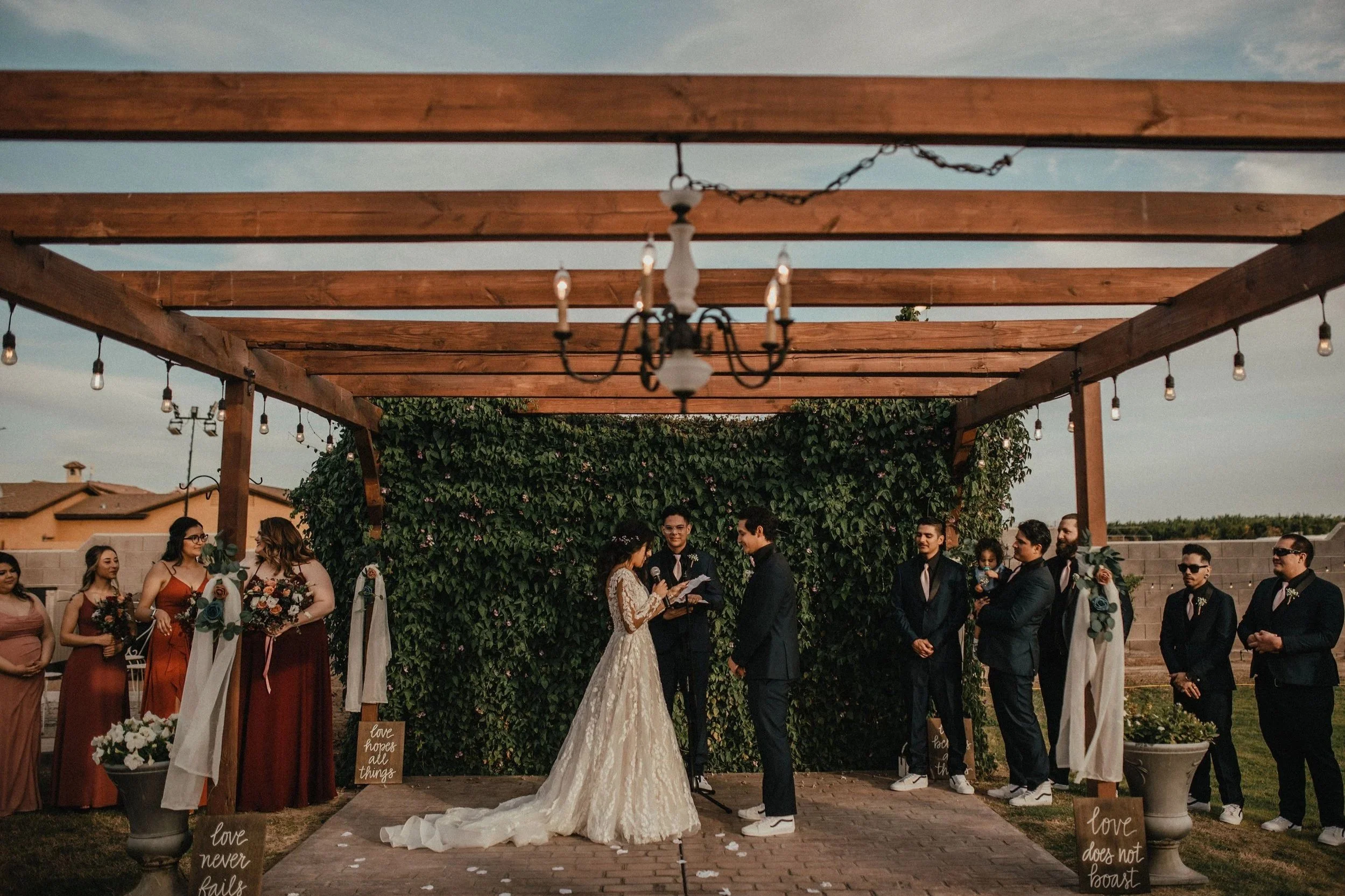 Bride and groom exchanging vows beneath the pergola during an outdoor wedding ceremony at Villa de la Meza in Yuma, Arizona.
