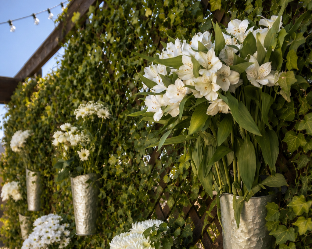 Hanging flower arrangements with white lilies, daisies, and chrysanthemums on a wooden lattice wall decorated with ivy