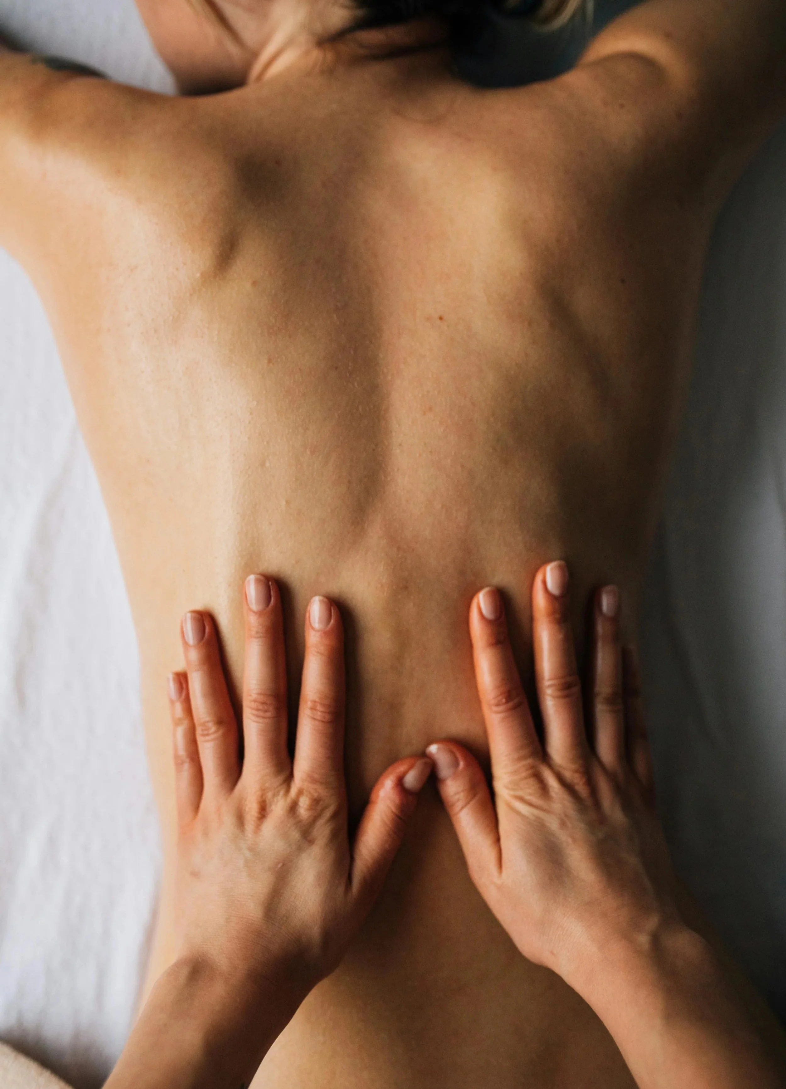 A person receiving a massage, lying face down on a massage table with hands applying pressure on their back.