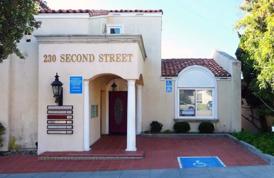 Building with a sign reading 230 Second Street, with a wheelchair accessible parking space in front, a decorative window, and a small garden area.
