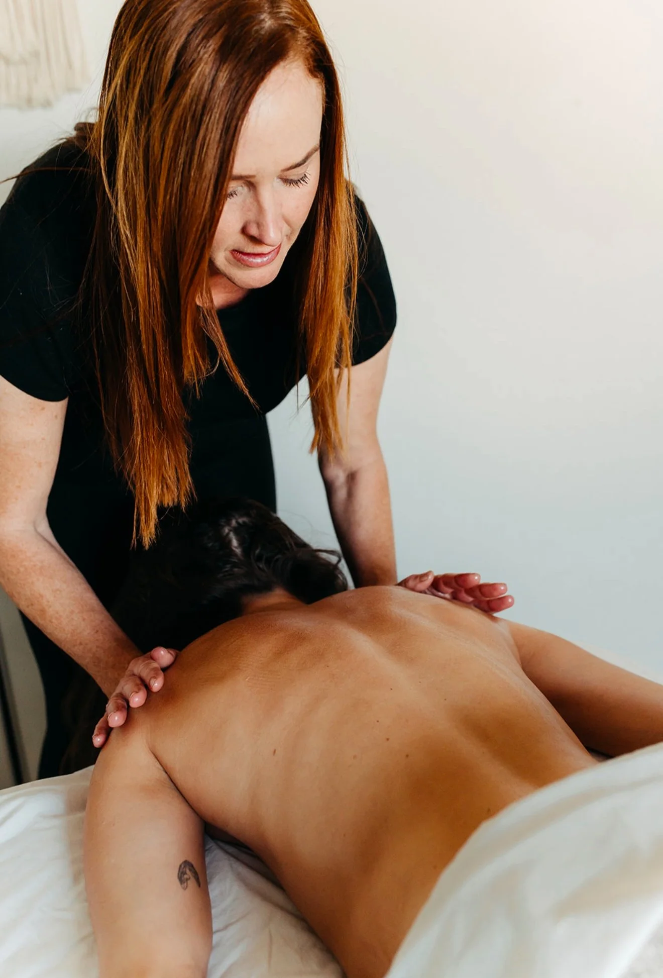 A woman providing a massage to a person lying face down on a massage table.