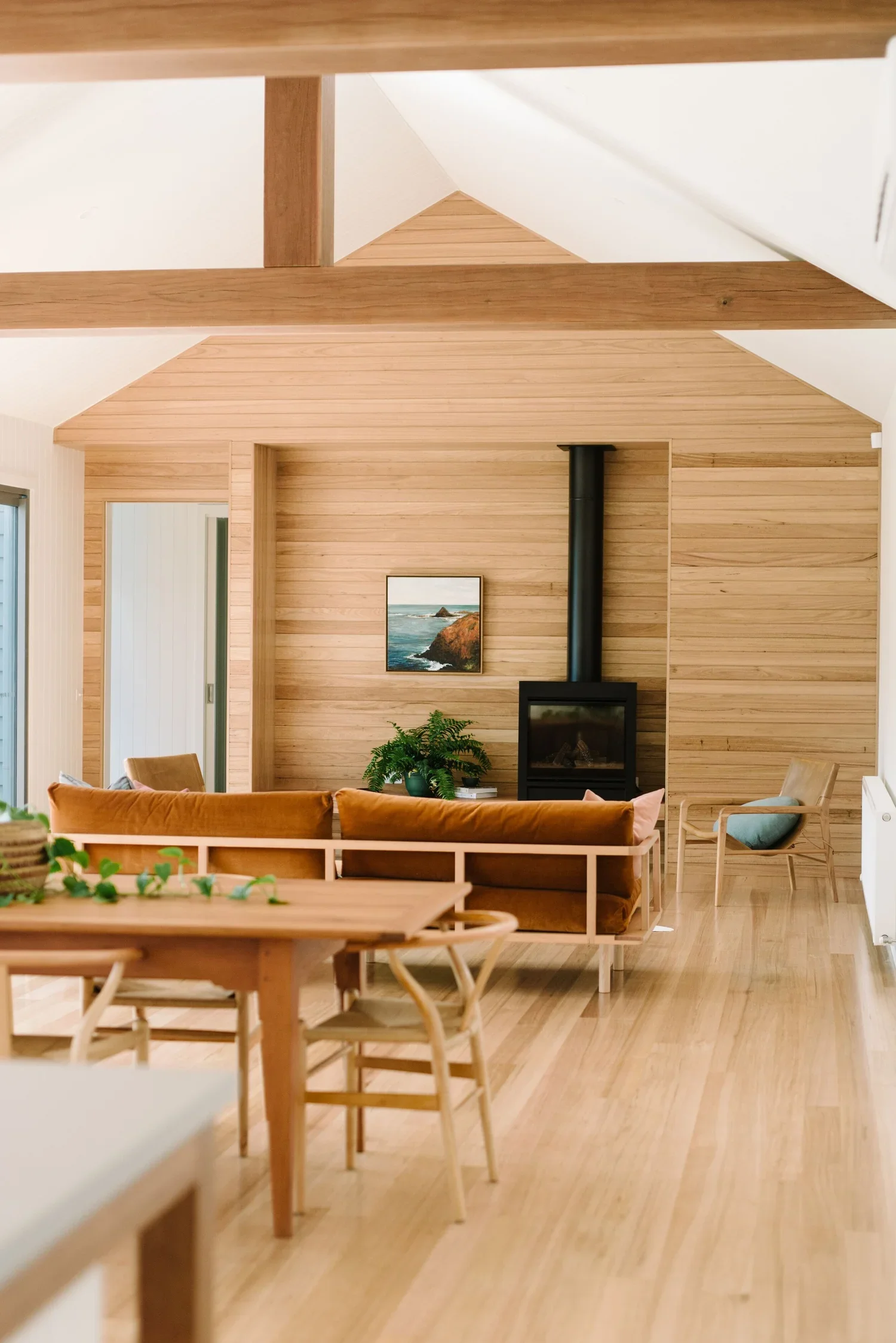 Interior living room with wooden walls, a wood-burning stove, framed coastal artwork, and various chairs and sofas.