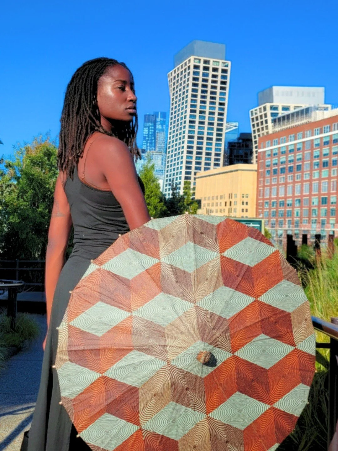 She moves through the city in grounded rhythm, carrying the Copper Parasol like a source of living current. Warm earth tones and spiraling geometry echo the metal&rsquo;s conductive nature, allowing her energy to flow, circulate, and return to center