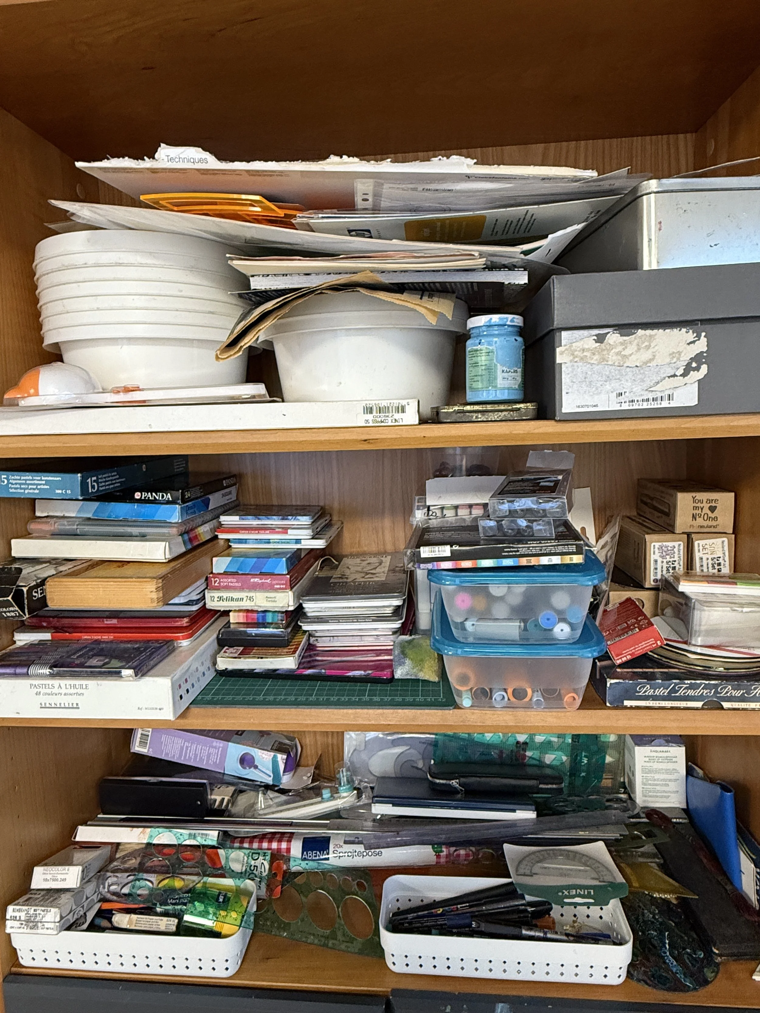 Organiseret skuffe med kunstnermaterialer, bøger, beholdere med blyanter og saks, samt papirer og bokse.