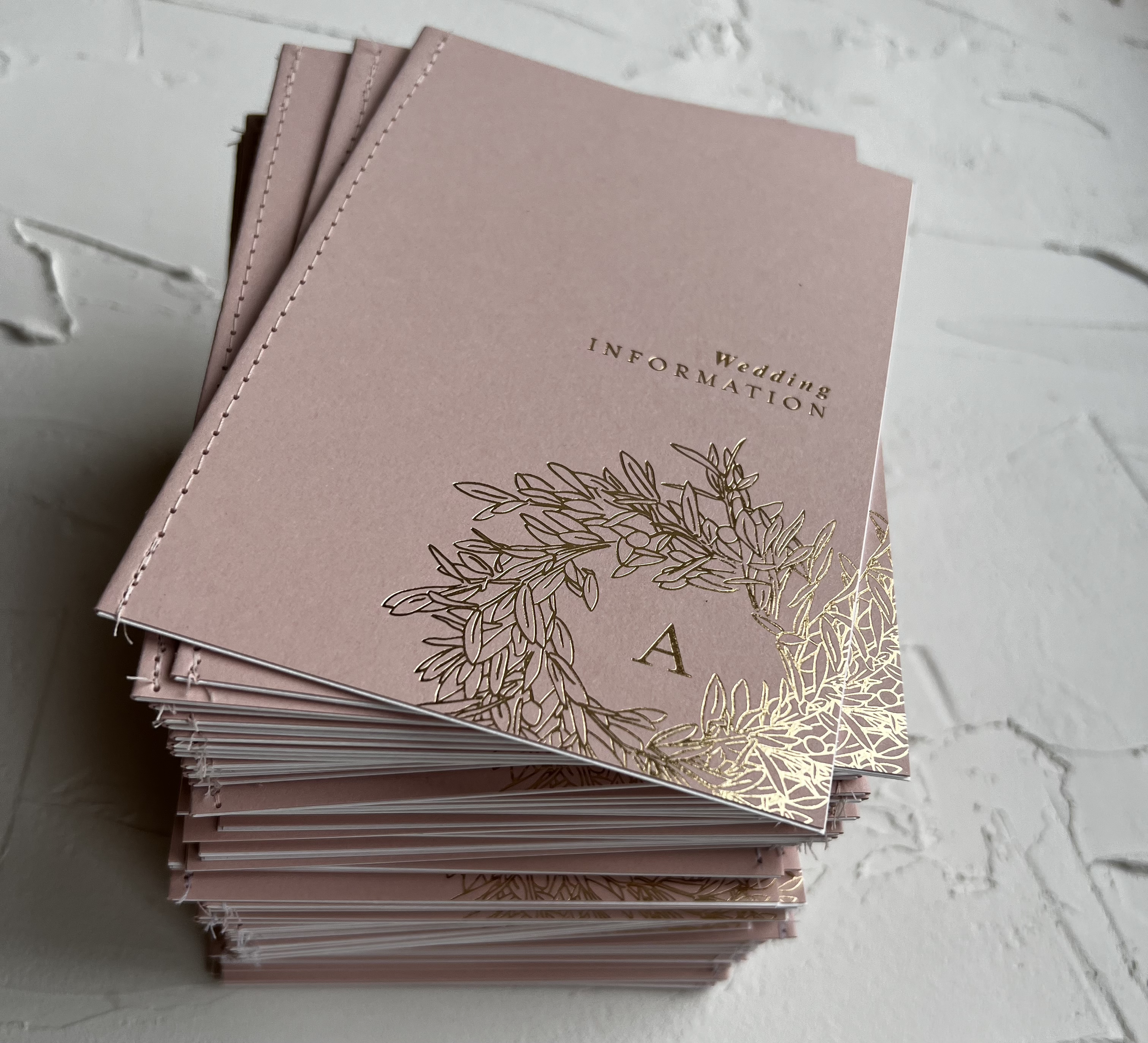 !0 page information booklets with a gold hot foiled cover and sewn down the spine to bind