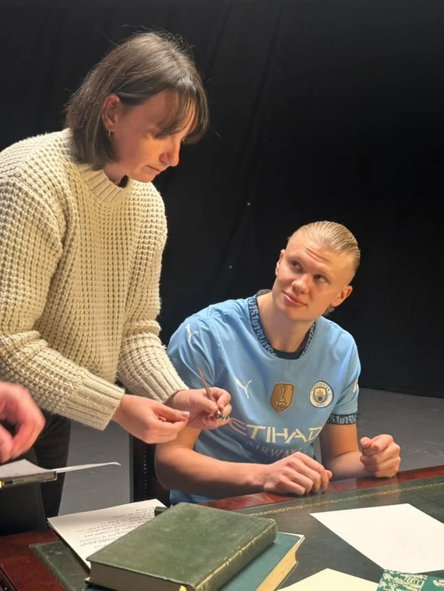 Showing Erling Haaland how to hold the calligraphy pen so it seems that he is writing the letter