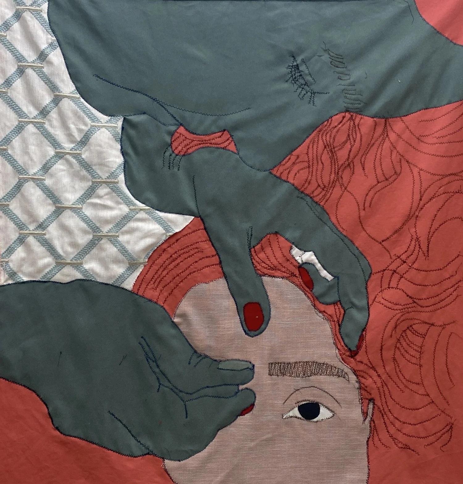 Lightly-wrinkled textile portrait: color-blocked fabrics pieced together with zigzag-stitch line work. A dark green figure with red nails carefully threads the thick brows of a redhead with voluminous hair. A quilt-like pattern fills the background.