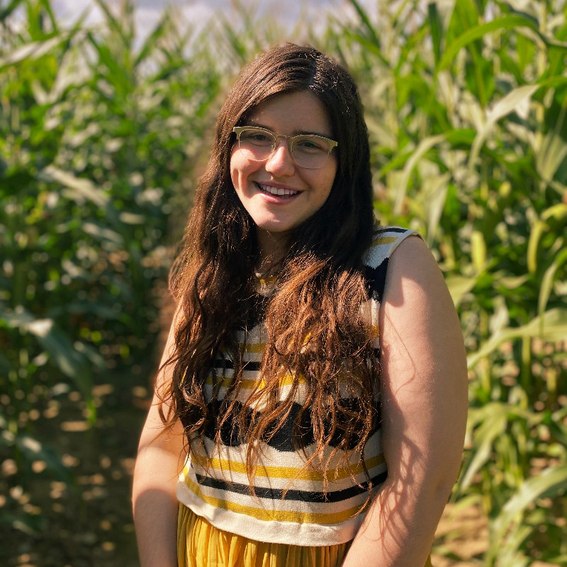 A white brunette woman smiles in a cornfield.