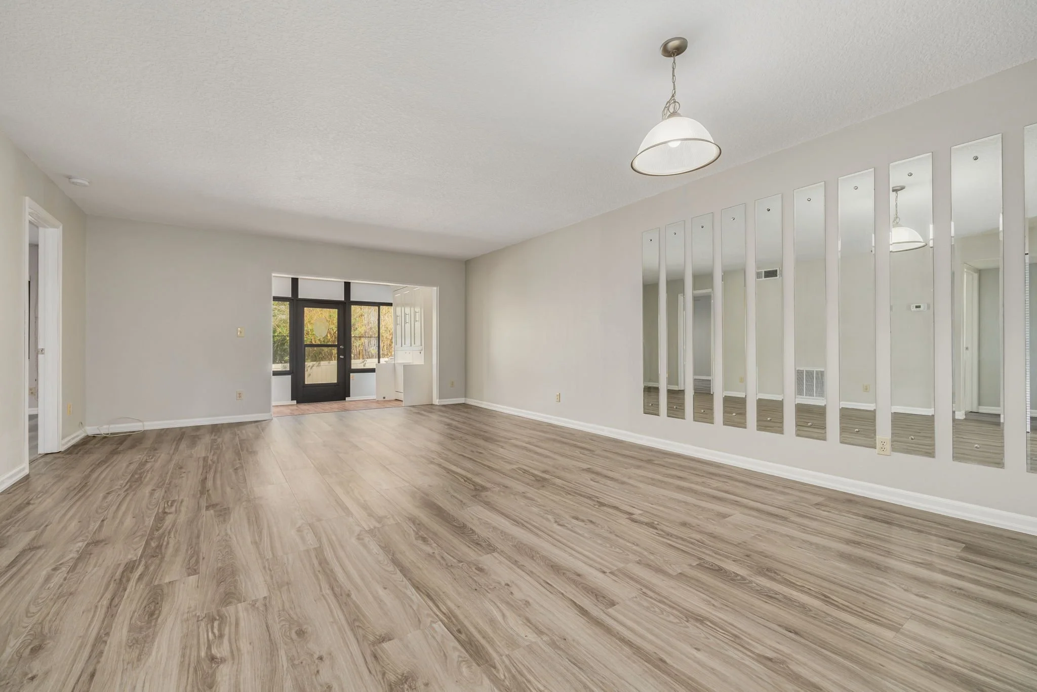 an empty living room with mirrors on the wall and a view to the backyard