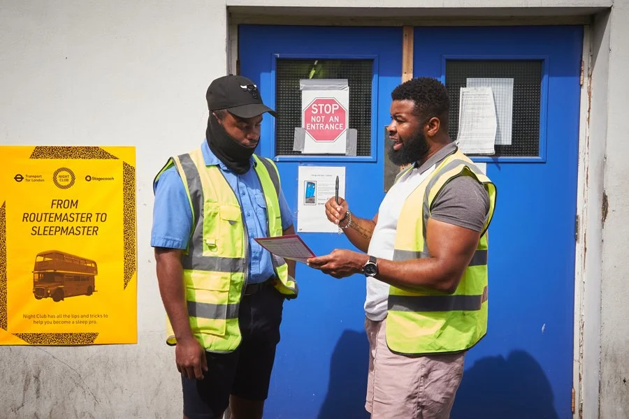 Two men in yellow hi-vis vests standing outside a blue door, engaged in conversation. One man is holding a clipboard. 