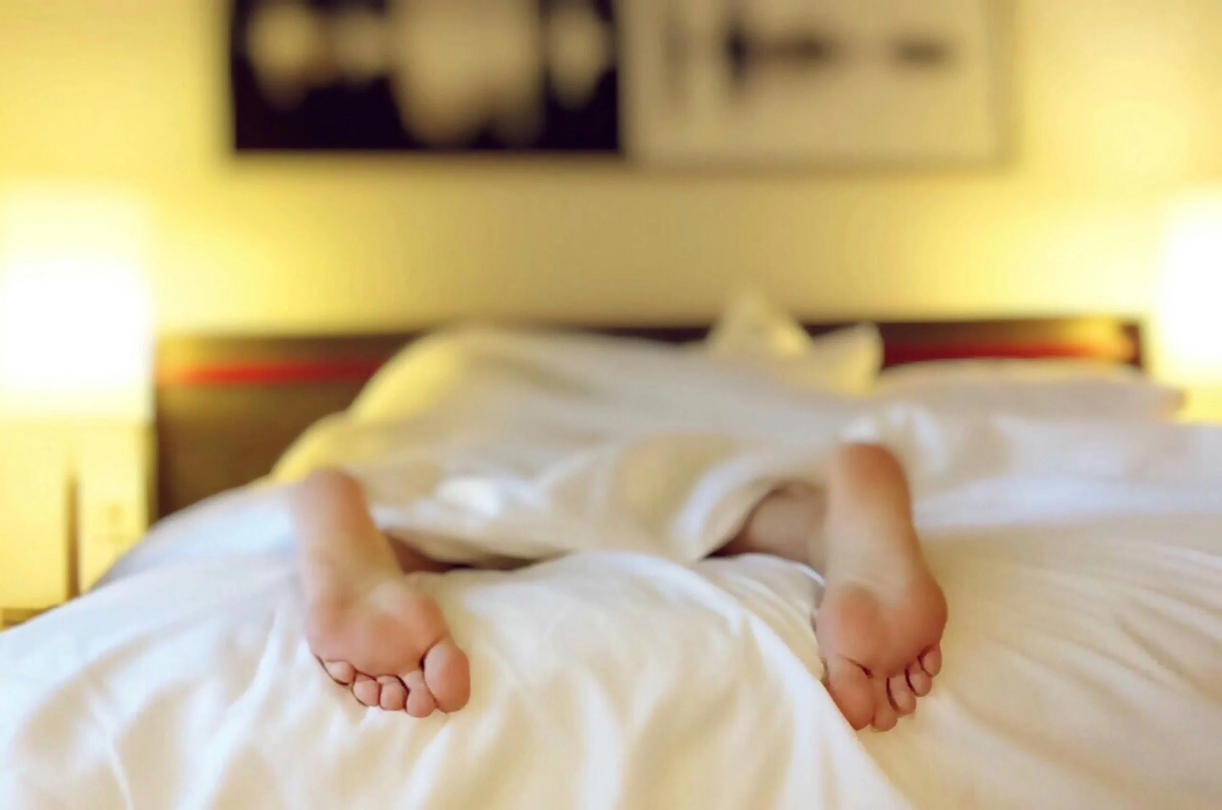 Two feet stick out of the bottom on the bed covers on a bed, presumably showing someone who is asleep