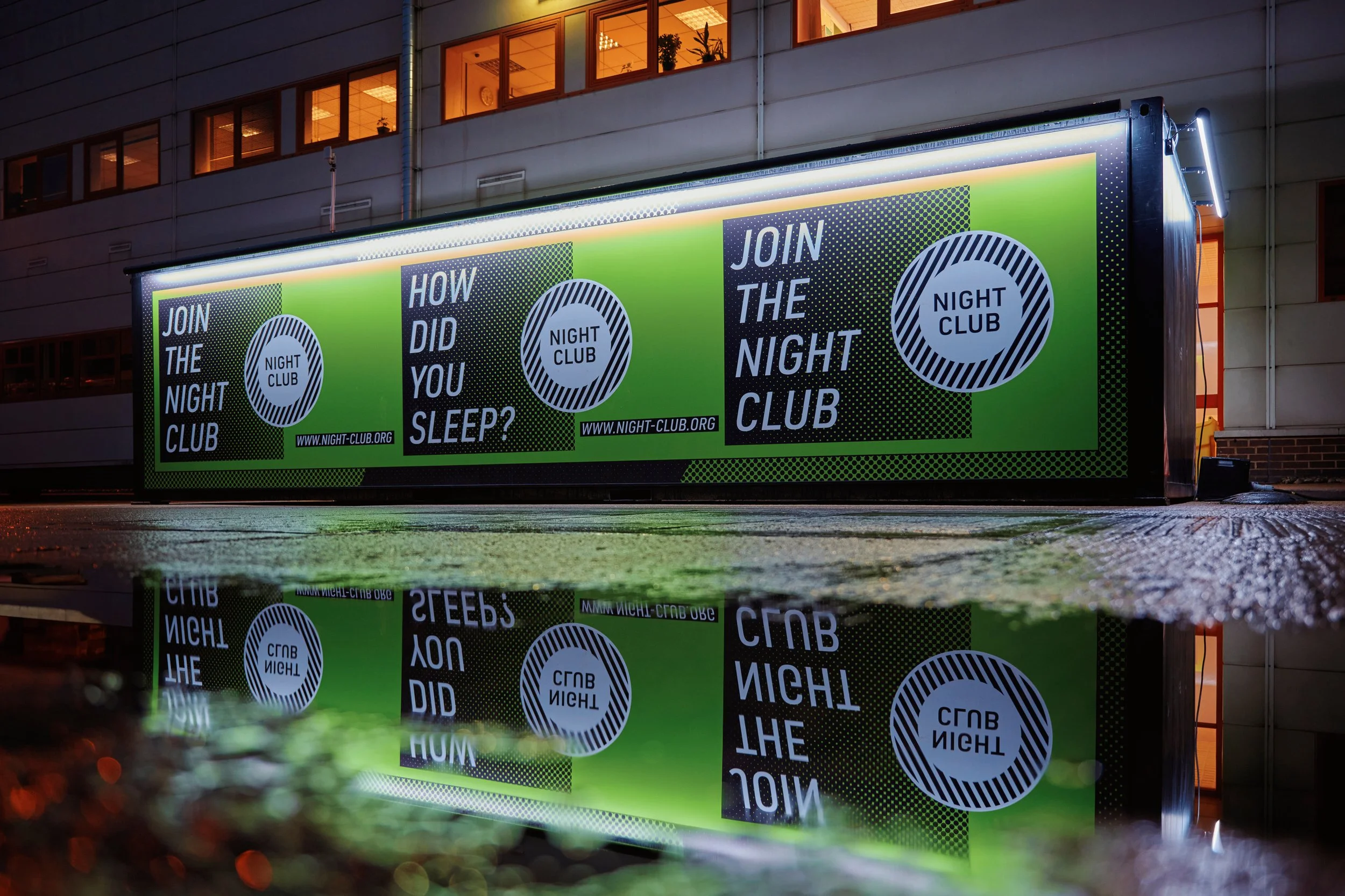 Backlit advertisement board outside a building promoting a night club, with green, black, and white graphics and text reading "Join the Night Club" and "How did you sleep?"