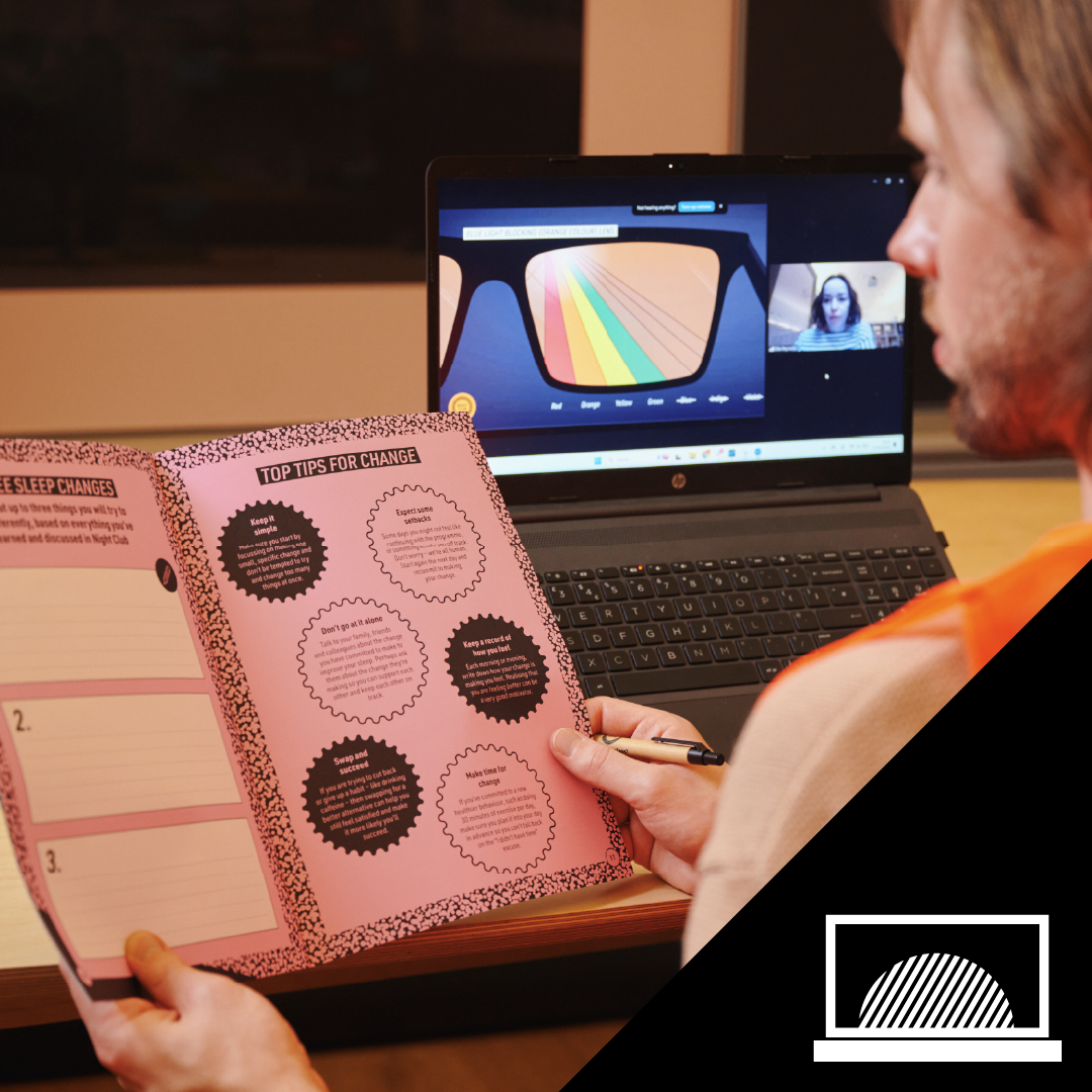 Person reading a pink booklet with tips for change at a desk in front of a laptop during a video call.